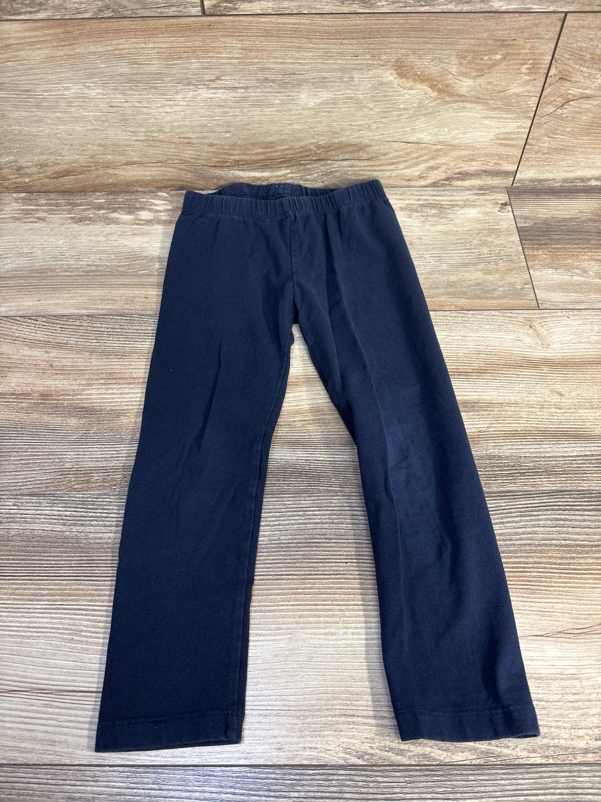 Flat lay of Baby Gap navy toddler leggings size 4T showcasing elastic waistband and straight legs with a wood floor background