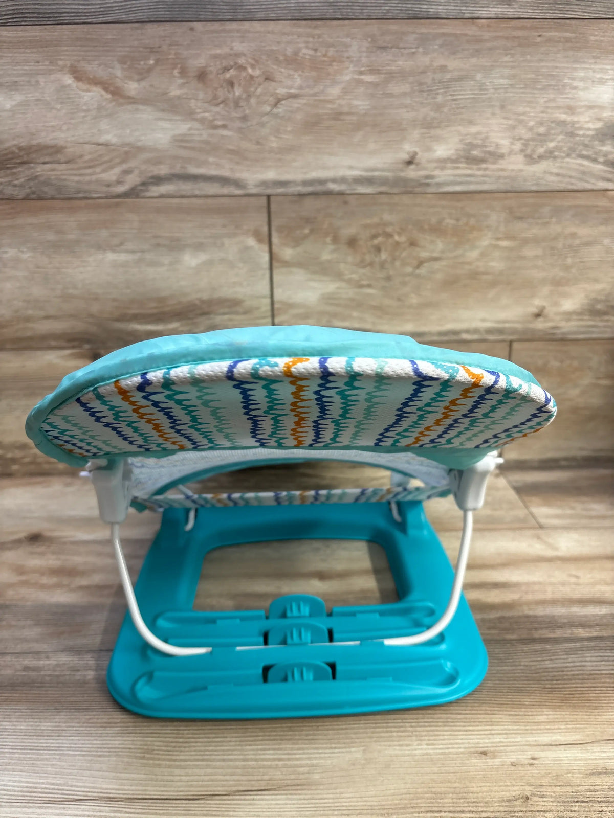 Front view of Summer Deluxe Baby Bather in green showcasing a patterned padded seat with a wood plank background