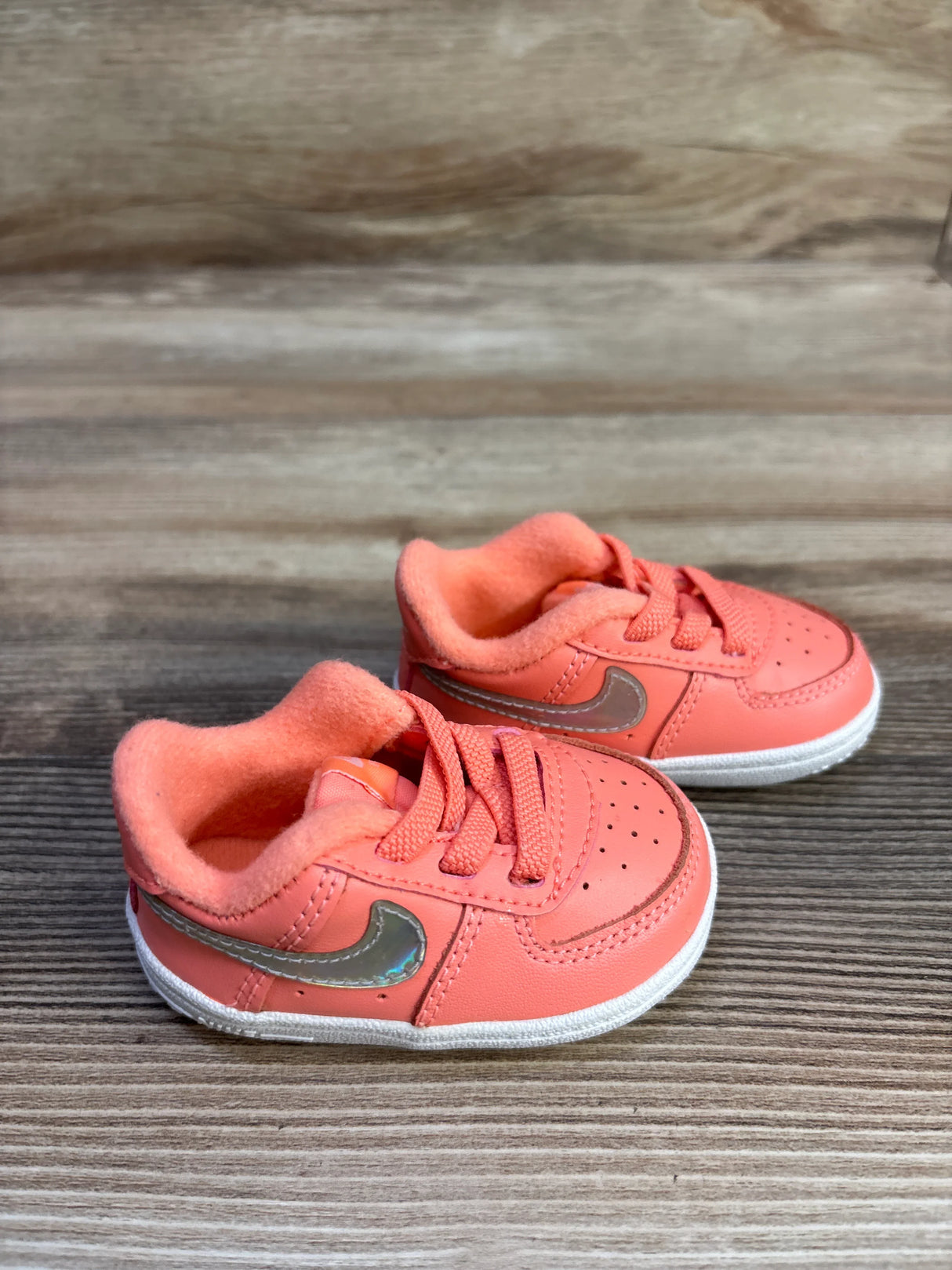 Angled front of Nike Force 1 CB sneakers size 2C in atomic pink with metallic Swoosh and white sole on wood