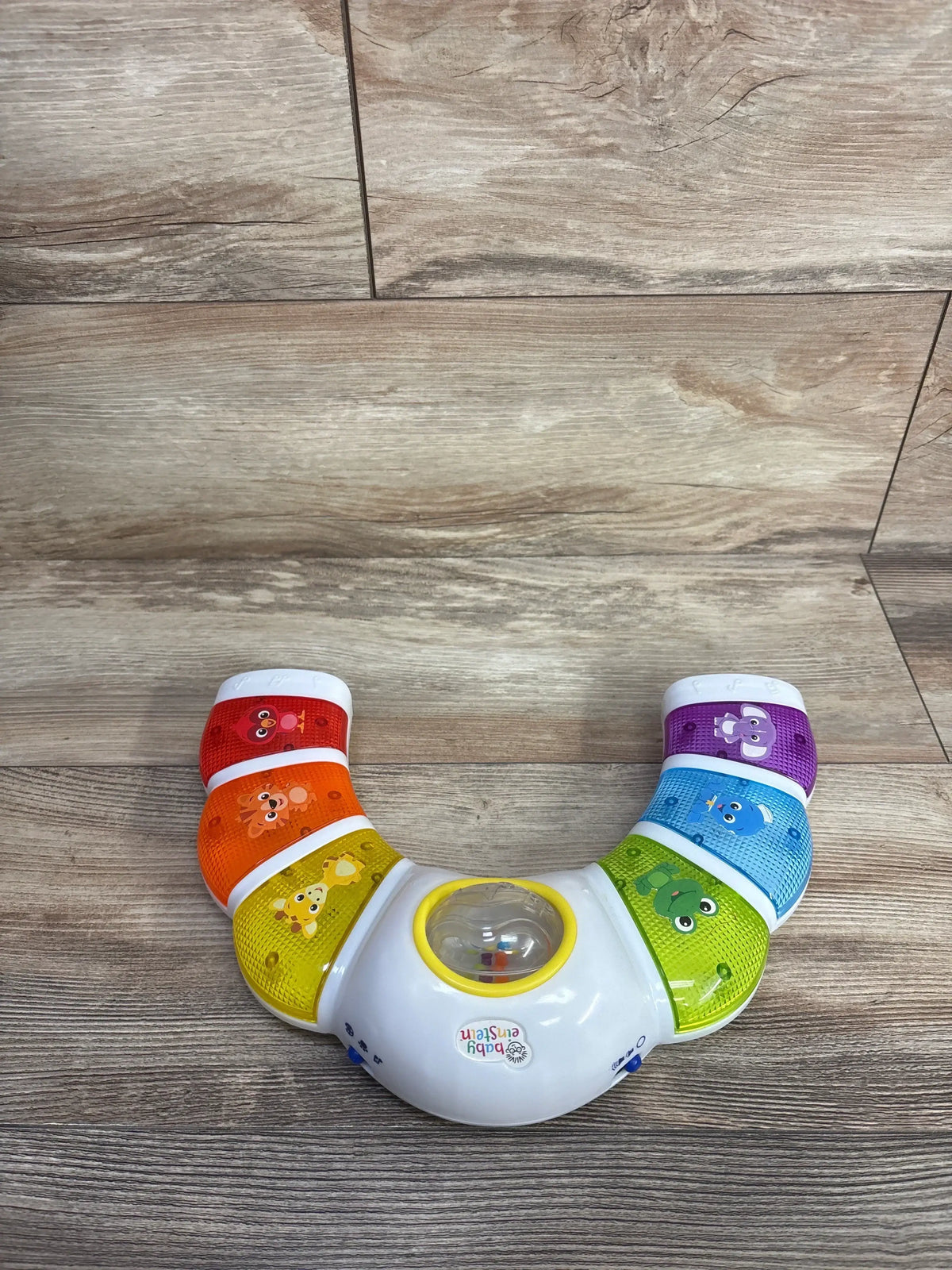 Top view of Baby Einstein Glow & Discover Light Bar showing colorful animal-themed sections and central rattle drum on a wood floor