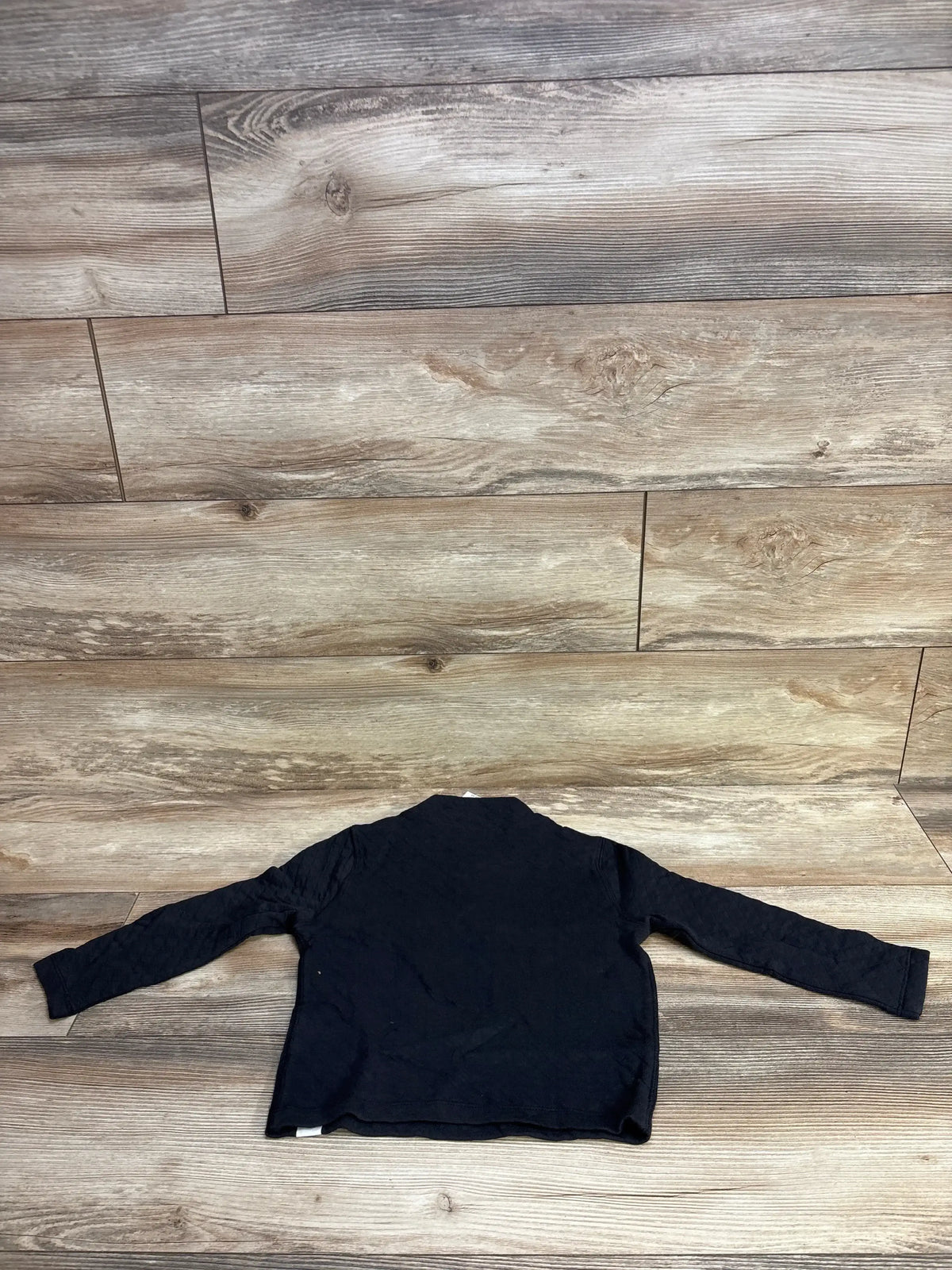 Back view of Baby Gap quilted snap pullover size 4T showing black long sleeves and quilted texture laid flat on wood floor