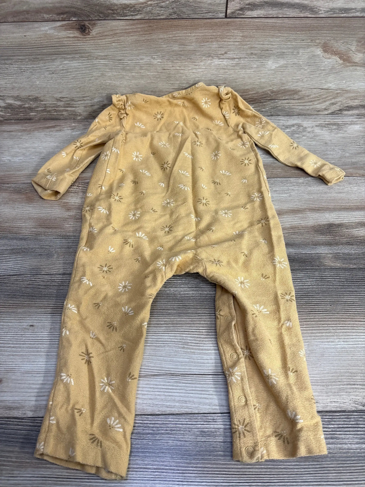 Yellow baby onesie with white and brown floral pattern laid flat on wooden surface