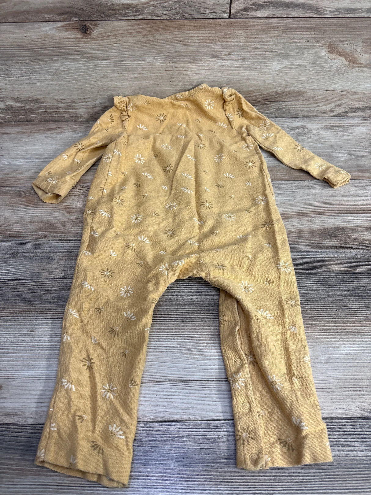 Yellow baby onesie with white and brown floral pattern laid flat on wooden surface