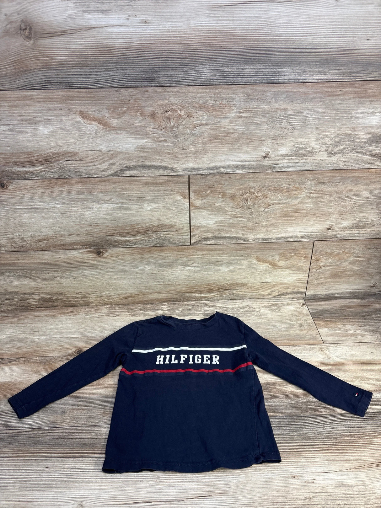 Navy blue long-sleeve Tommy Hilfiger shirt with white and red stripes on wood floor