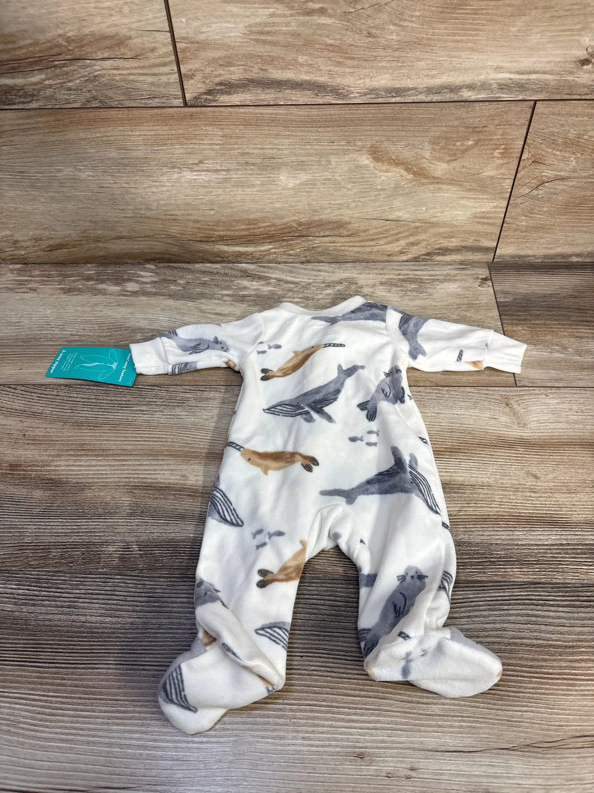 Top view of white Child Of Mine blanket sleeper in preemie size with long sleeves and whale print on a wood-look floor