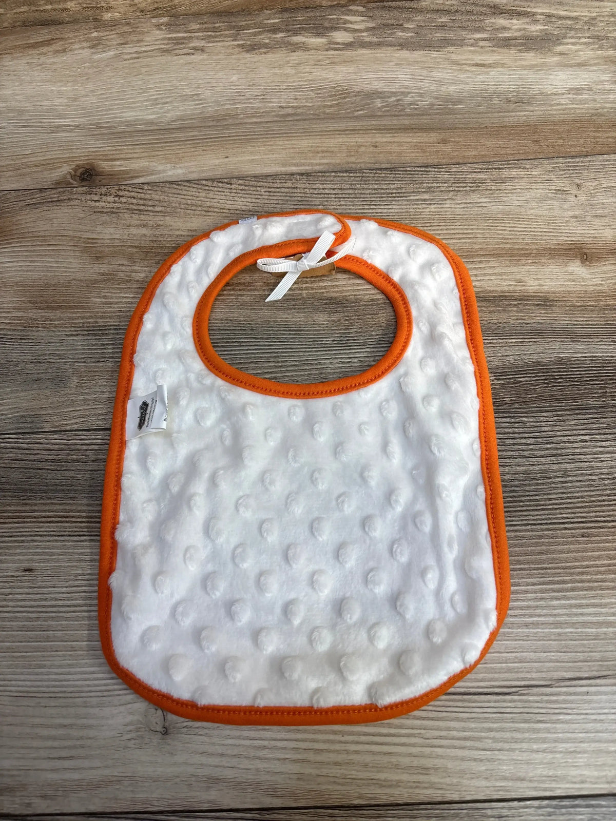 White textured baby bib with orange trim on wood background