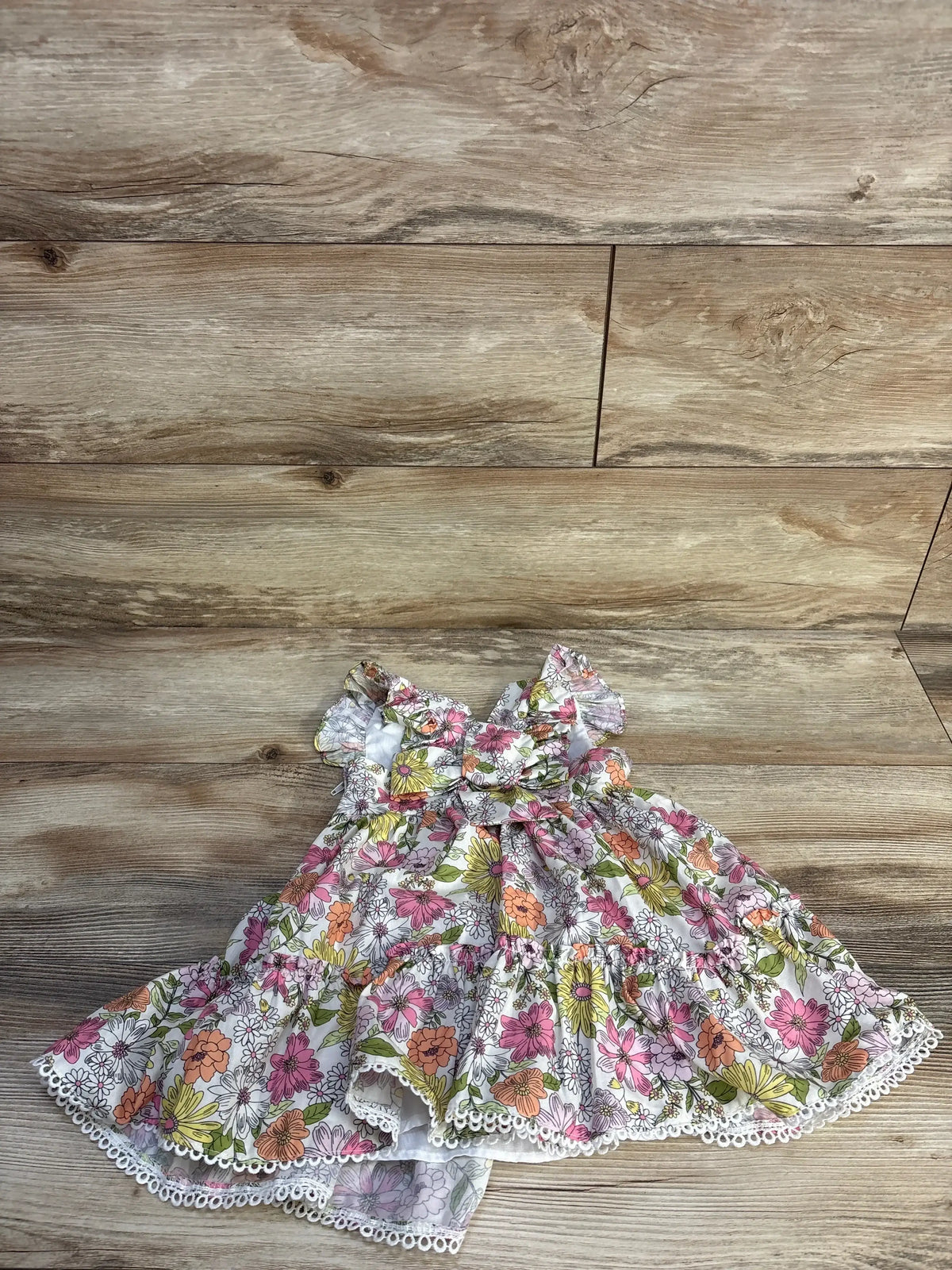 Flat lay of Rare Editions girls white floral dress size 2T showcasing ruffle sleeves, front bow and eyelet trim on wood background