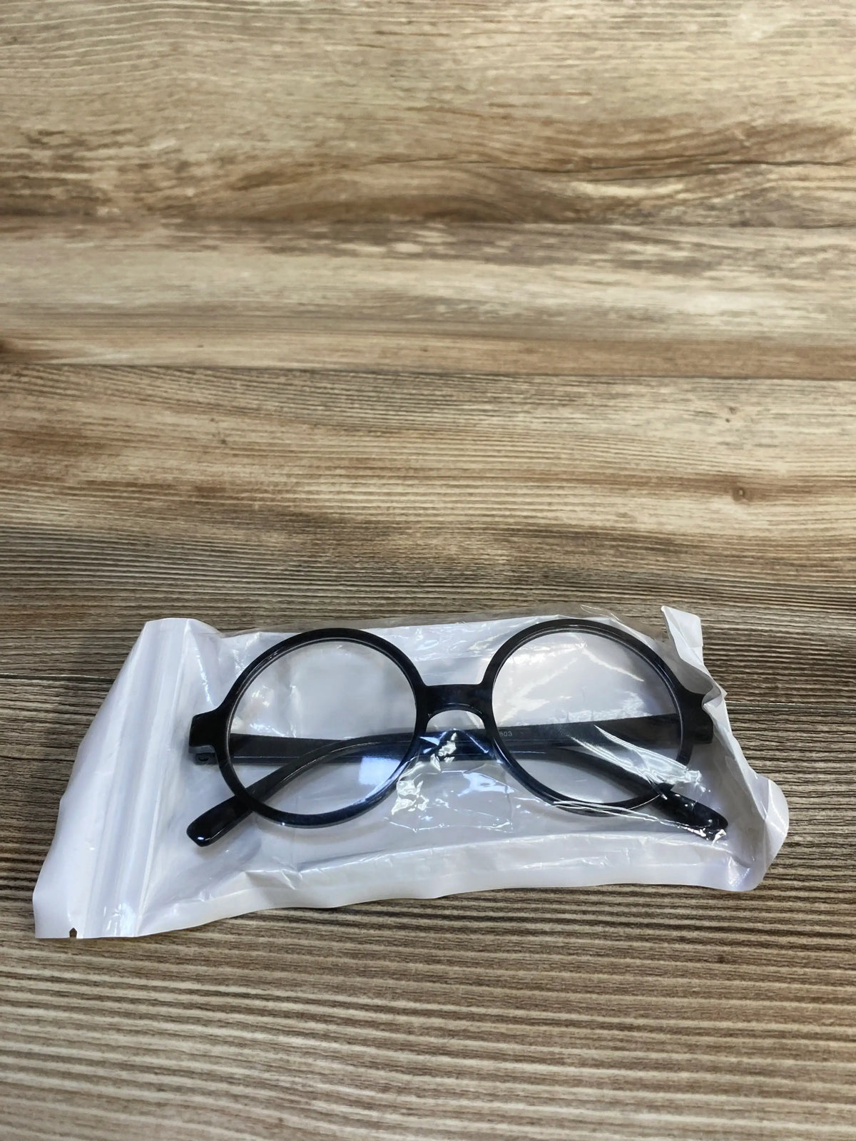 Round black eyeglasses inside clear plastic packaging on wood surface