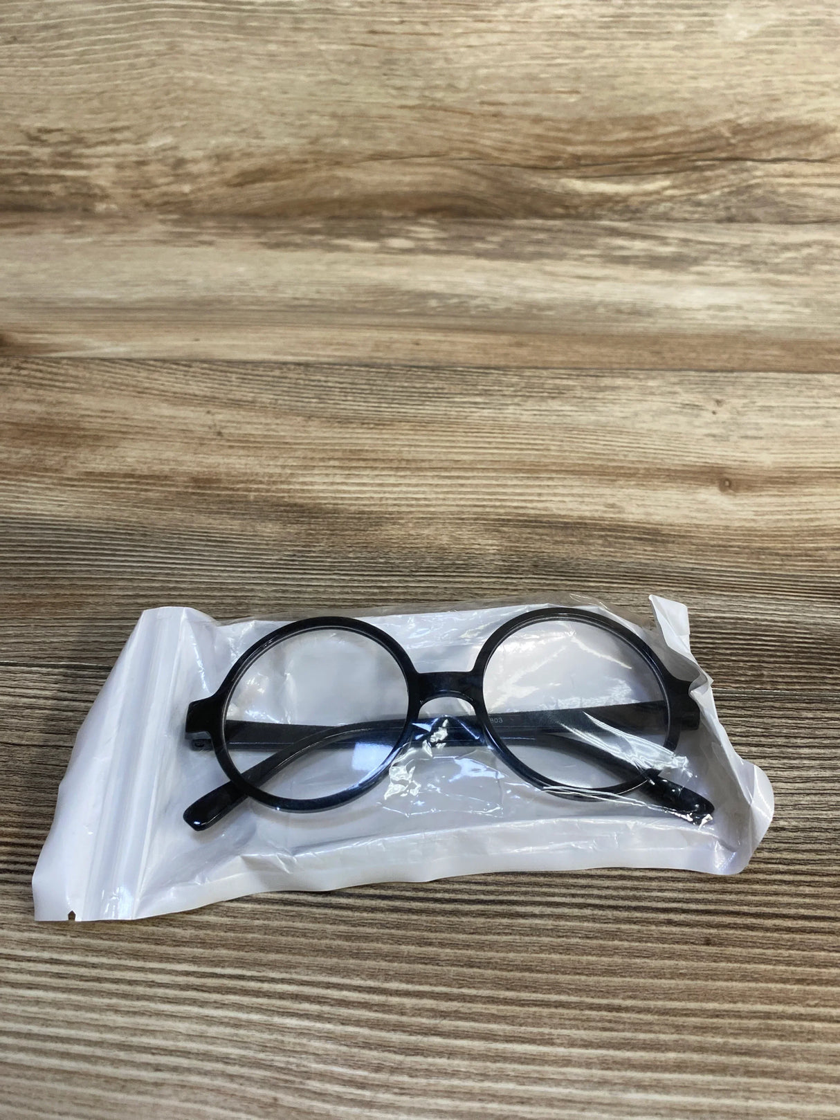Round black eyeglasses inside clear plastic packaging on wood surface