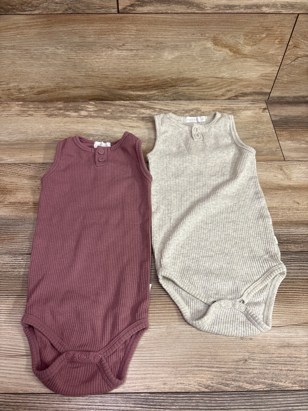 Jamie Kay pink and grey ribbed sleeveless henley bodysuits for toddlers laid on a wood floor.