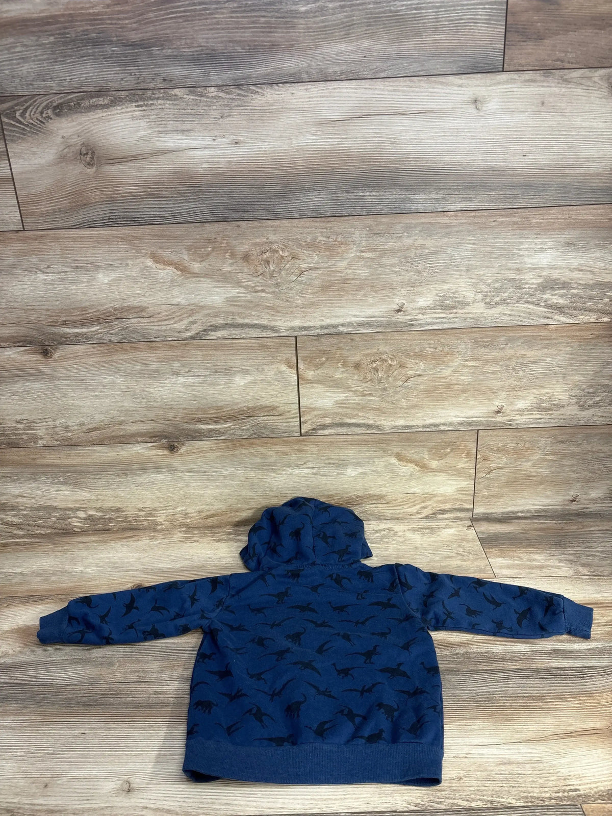 Blue kids hoodie with black dinosaur print, displayed flat on wood background