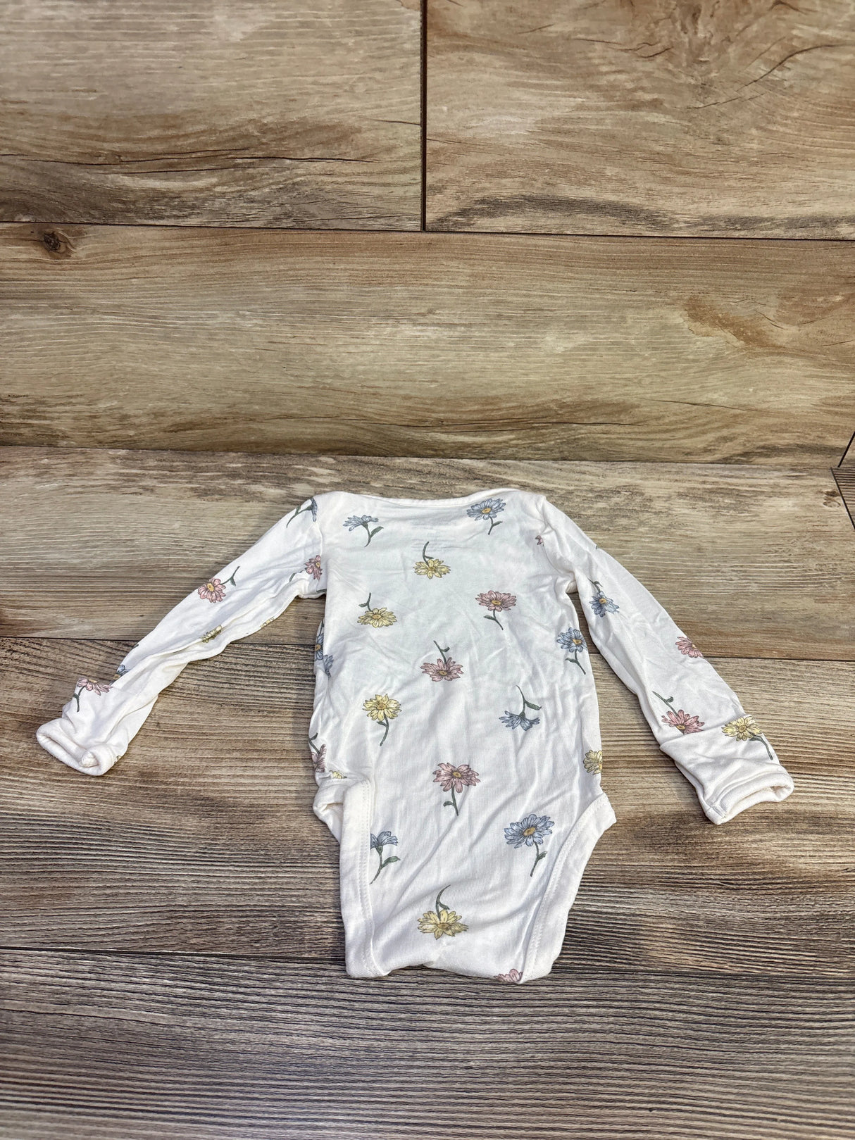 Flat lay of Carter’s PurelySoft white long-sleeve baby bodysuit with small pastel floral print and snap crotch on wood background