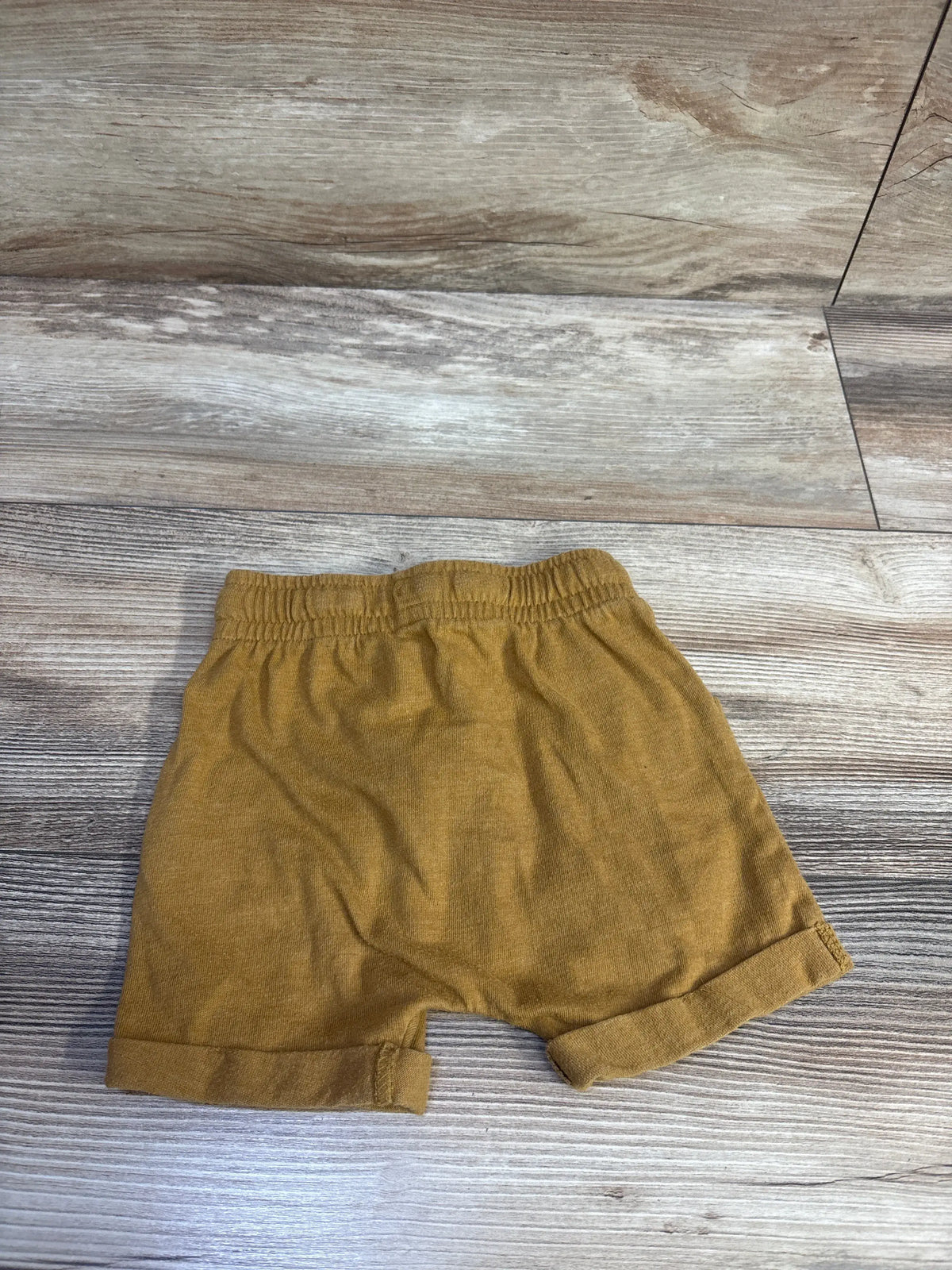 Front view of brown Cat & Jack drawstring shorts in size 12 months with an elastic waistband and cuffed hems on a wood floor
