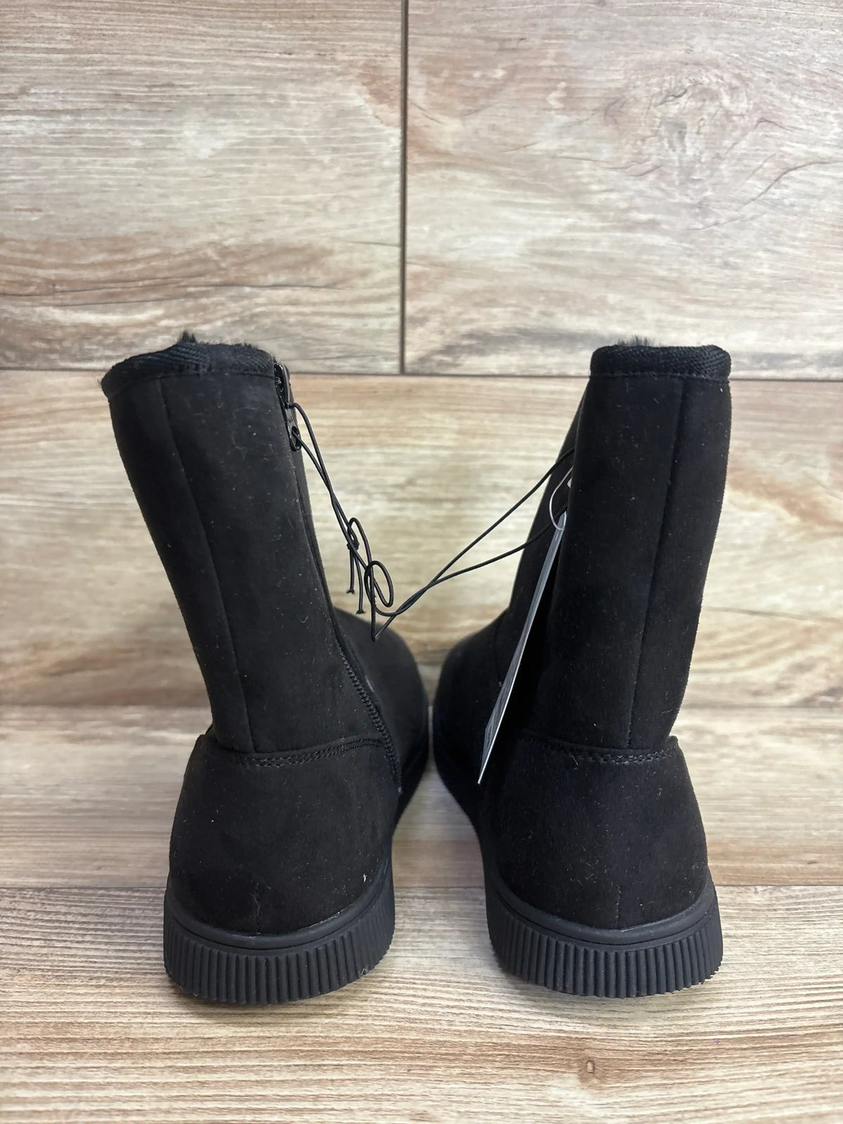 Back view of black suede kids' winter boots with rubber soles on wood floor
