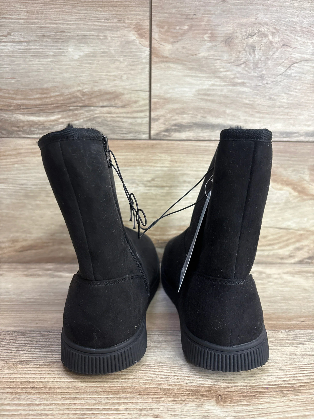 Back view of black suede kids' winter boots with rubber soles on wood floor