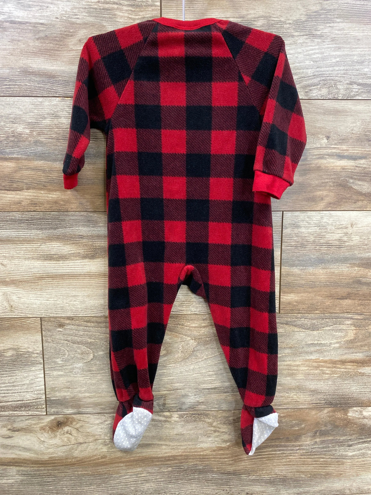 Red and black plaid baby footed sleeper with long sleeves on wood background