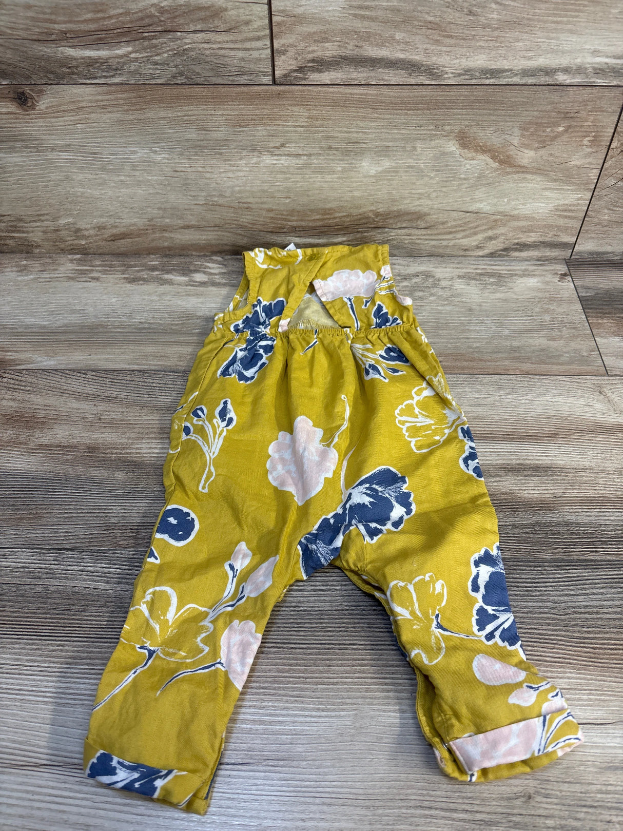 Yellow floral baby romper with blue and pink flower print on wooden floor
