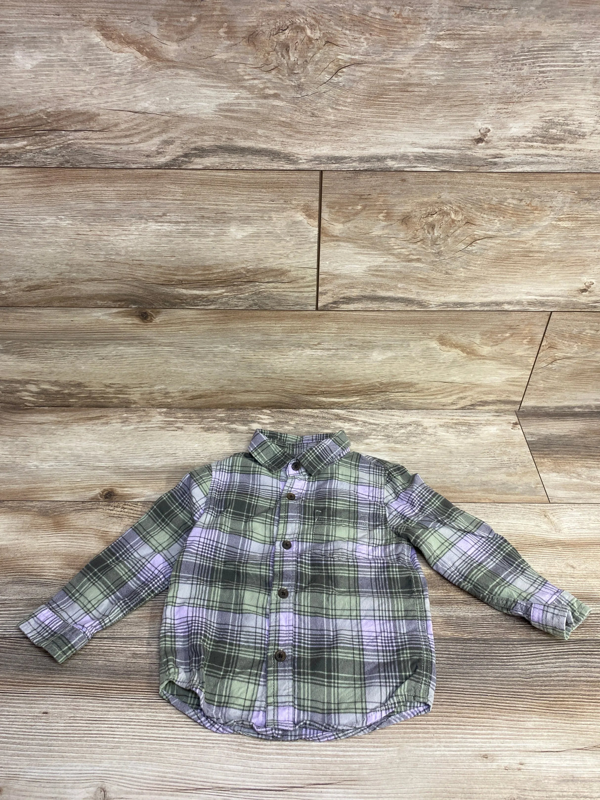 Children's green and purple plaid long-sleeve button-up shirt on wooden background