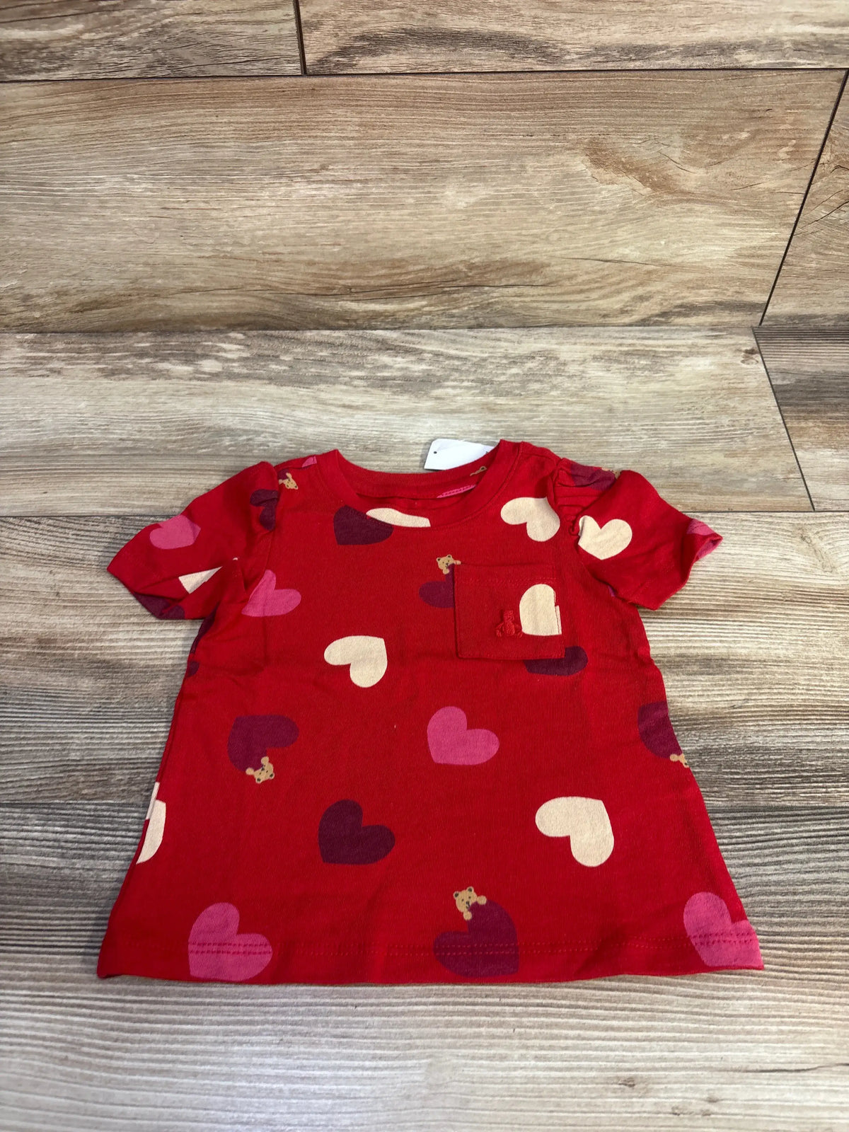 Front view of red Baby Gap puff sleeve pocket shirt with heart print on wood-look background