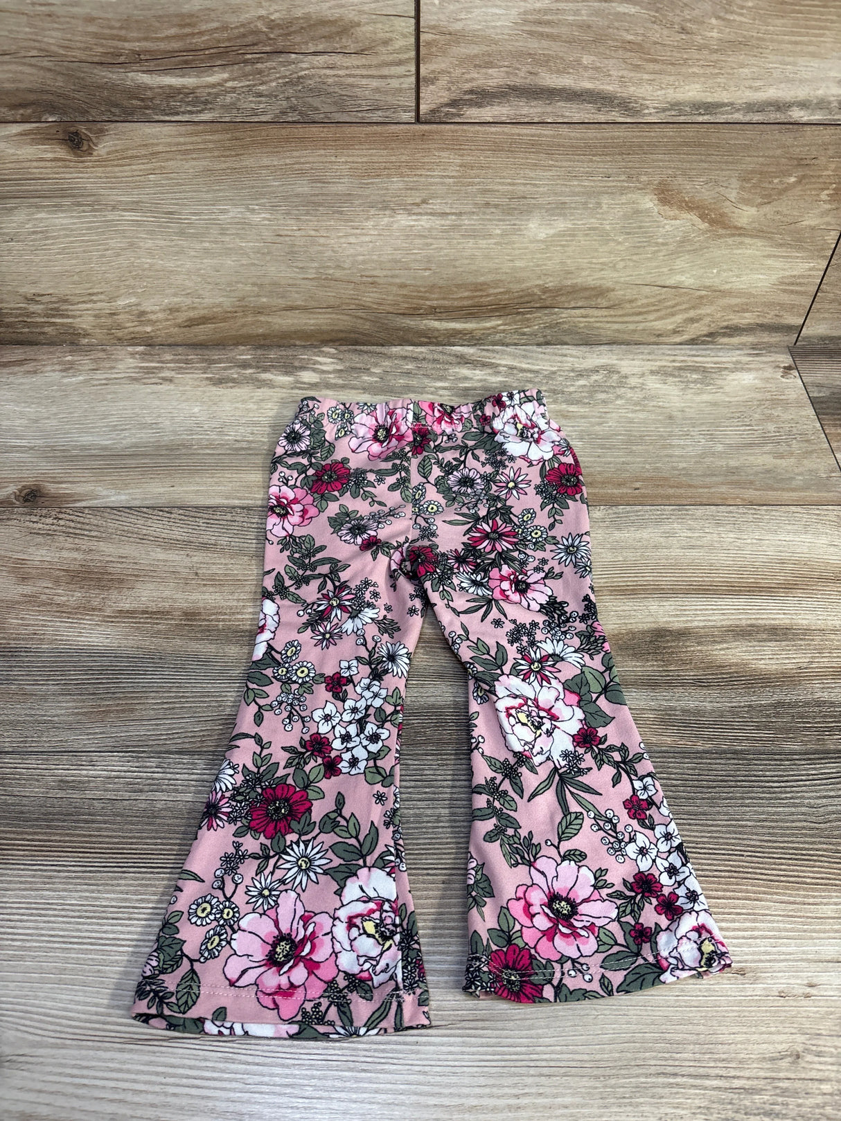 Flat lay of pink baby flare-leg leggings showcasing all-over floral print and elastic waistband on wood background