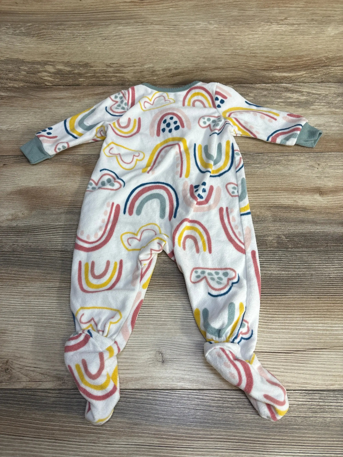 Flat lay of Carter’s rainbow-print footed blanket sleeper showcasing multicolor rainbows and mint cuffs on wood floor
