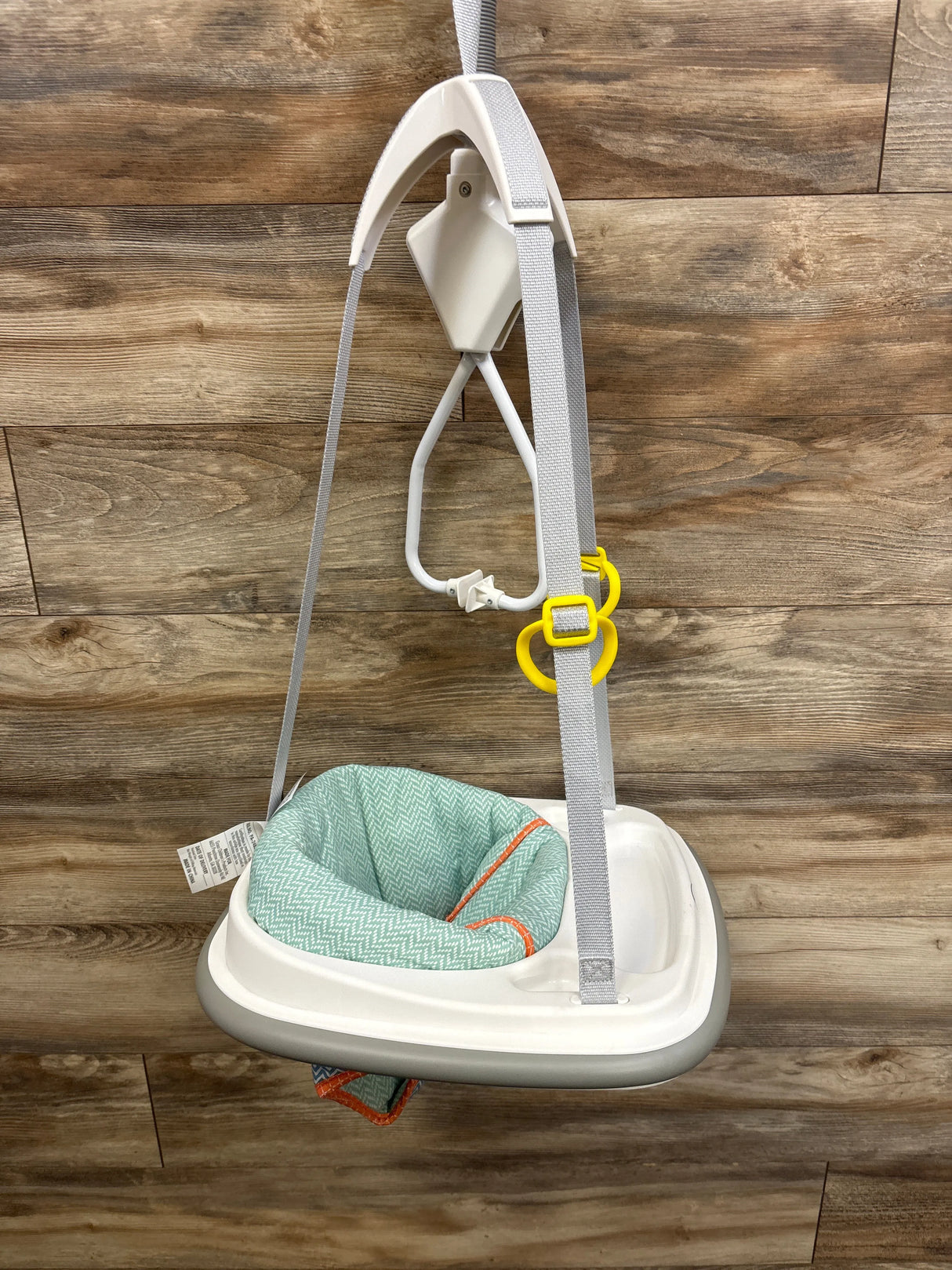 Front view of Graco Doorway Bumper Jumper Caravan showcasing mint green padded seat, white plastic frame, gray adjustable straps, and yellow adjustment clips against wood-paneled background
