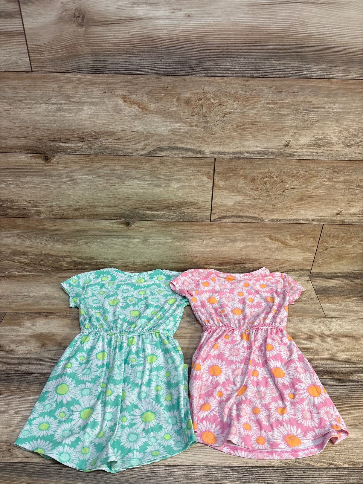 Flat lay of two 4T toddler dresses (2-pack) showing green and pink daisy prints with elastic waist on wood background