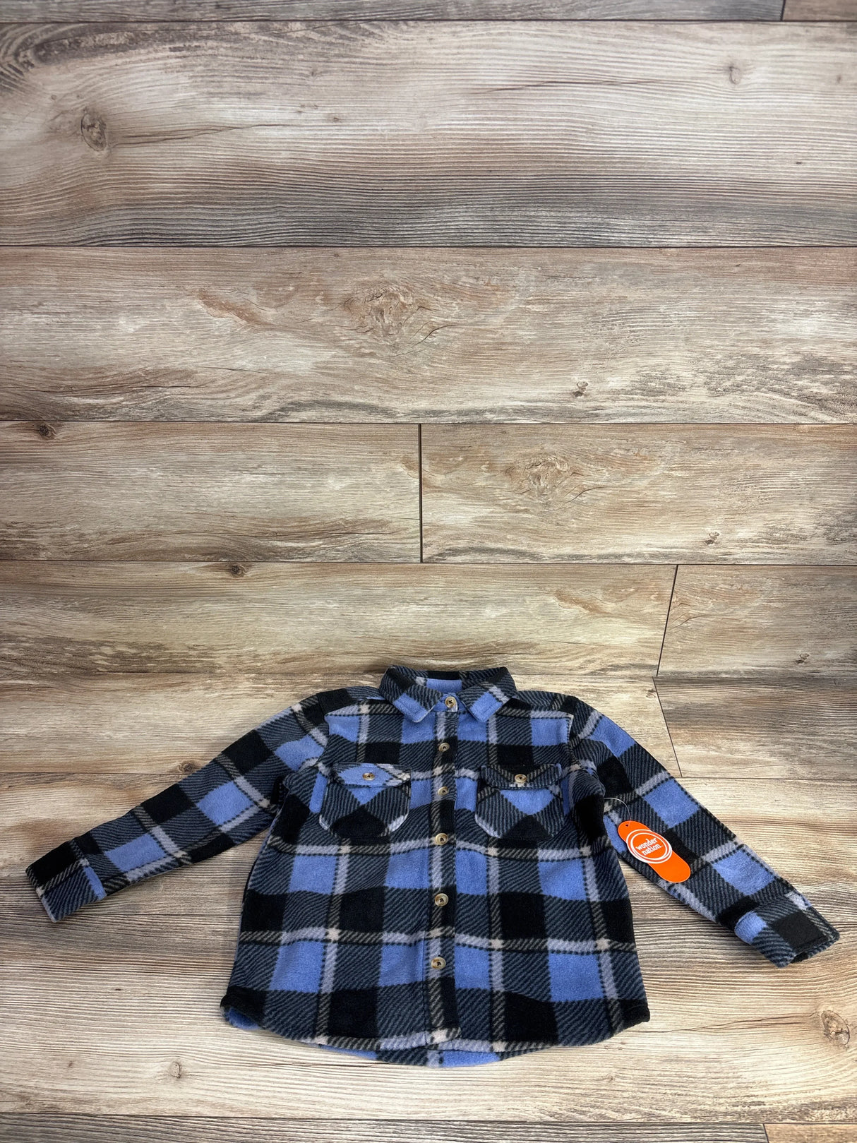 Blue and black plaid flannel long sleeve toddler shirt with front pockets on wood background