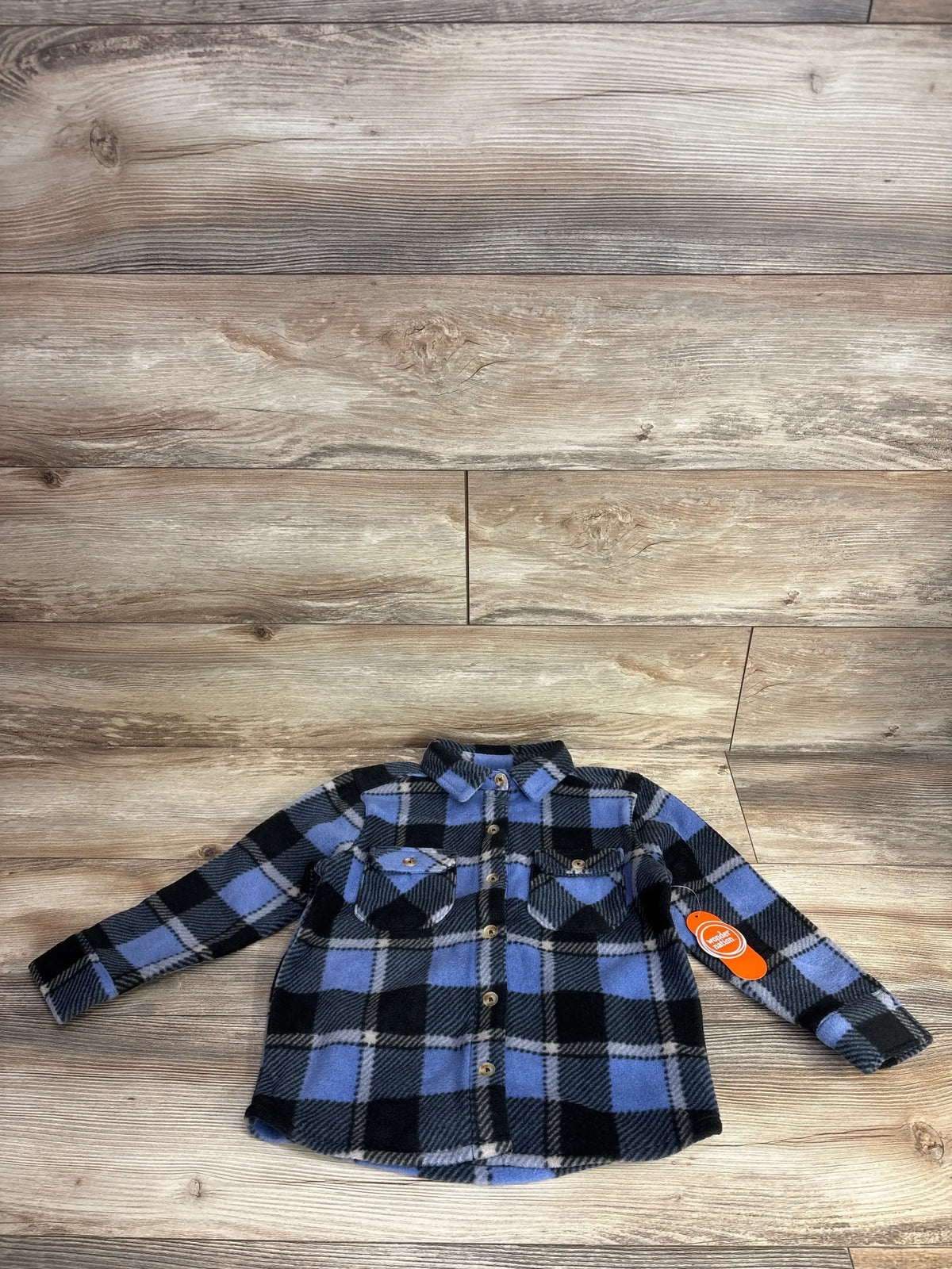 Front view of blue and black plaid fleece jacket showcasing button front and two chest pockets with wood background