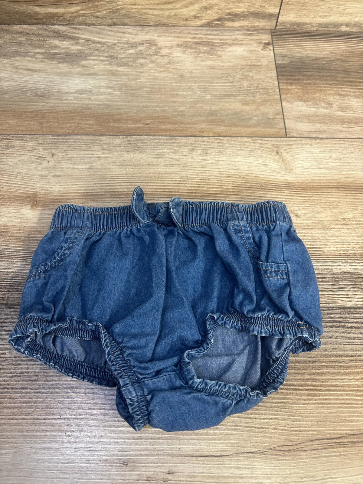 Front view of Cat & Jack blue chambray bloomers showcasing elastic waistband and leg openings on a wood-look floor