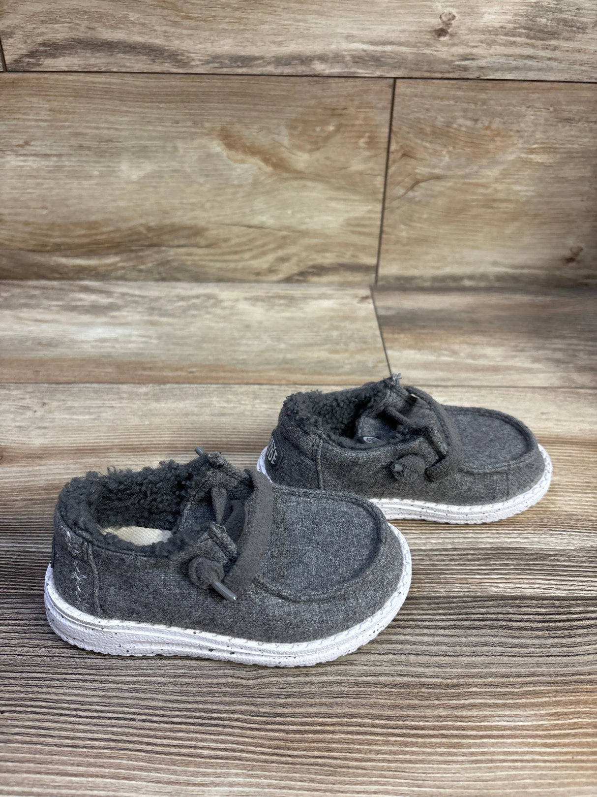 Three-quarter view of Hey Dude Wendy kids wool slip-ons with grey wool, sherpa lining, and white sole on wood background