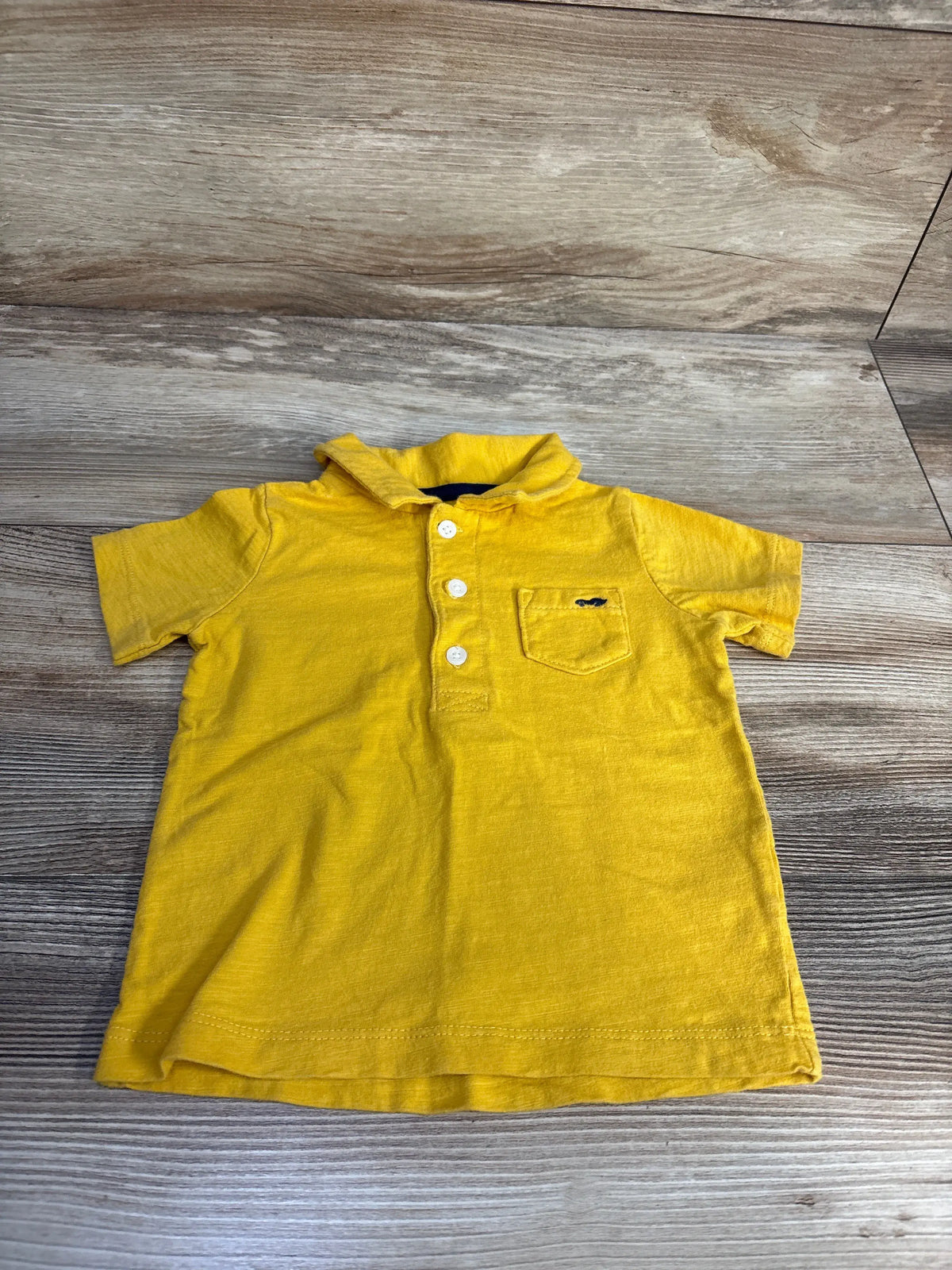 Front view of Carter’s yellow polo shirt showcasing a structured collar, button placket, and chest pocket on wood grain