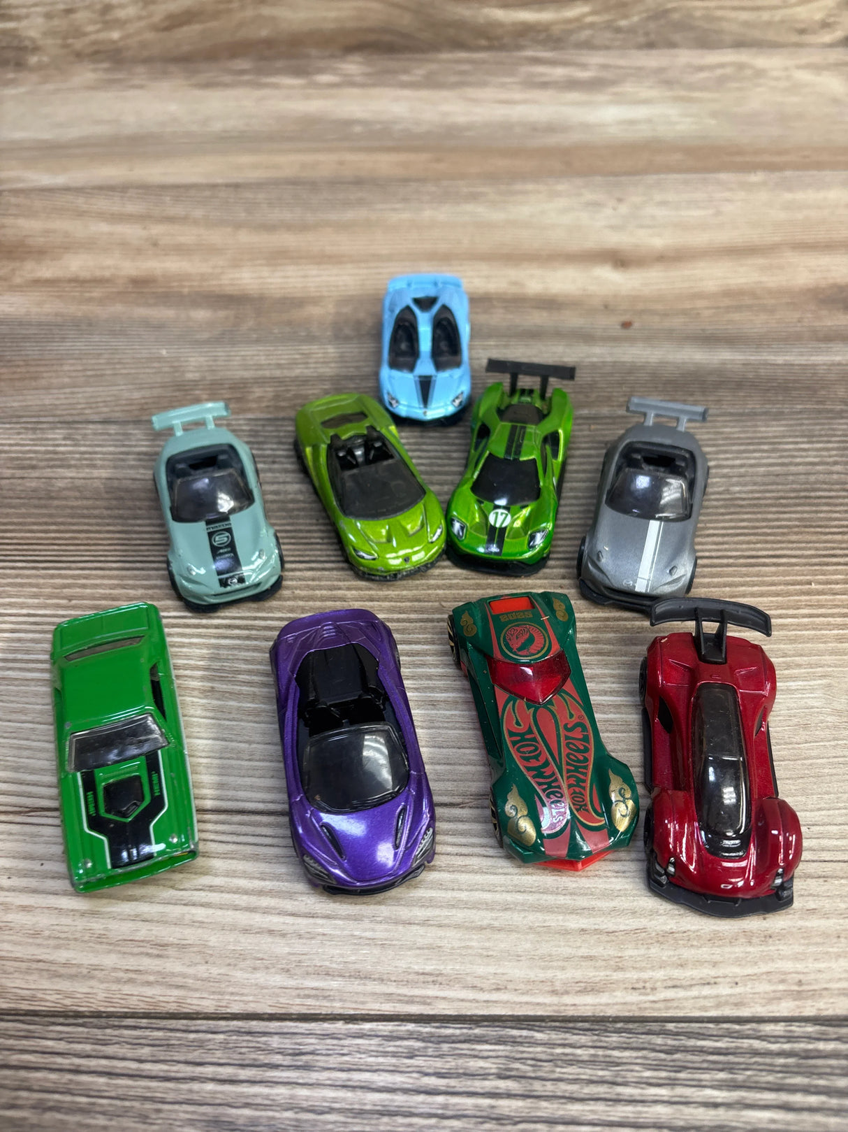 Collection of nine colorful Hot Wheels toy cars arranged on a wooden surface
