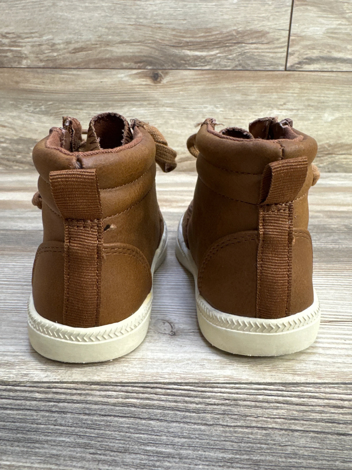 Rear view of Billy Footwear Harmon high-top sneakers in brown showing pull tabs and white textured soles on wood background