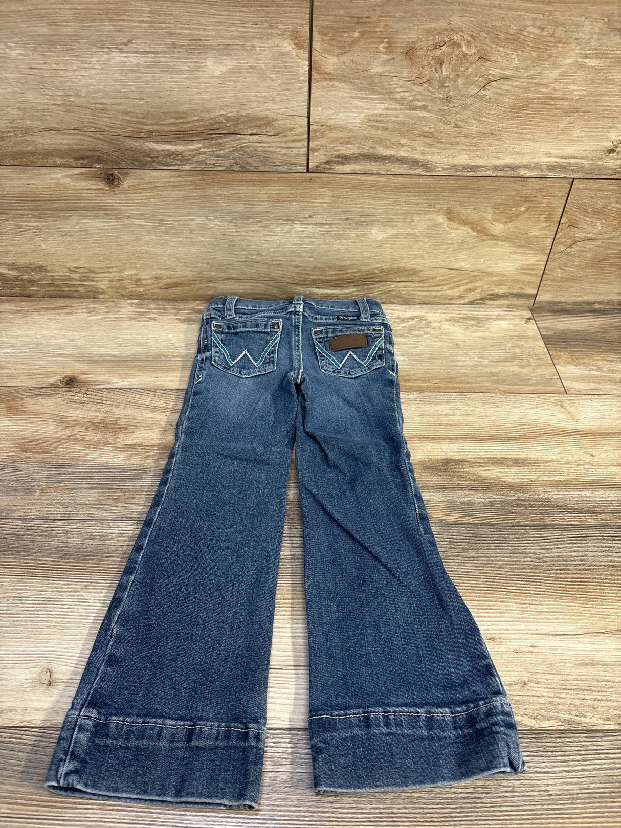 Back view of Wrangler slim flared toddler jeans in medium blue showing back pocket embroidery and flared legs on wood floor