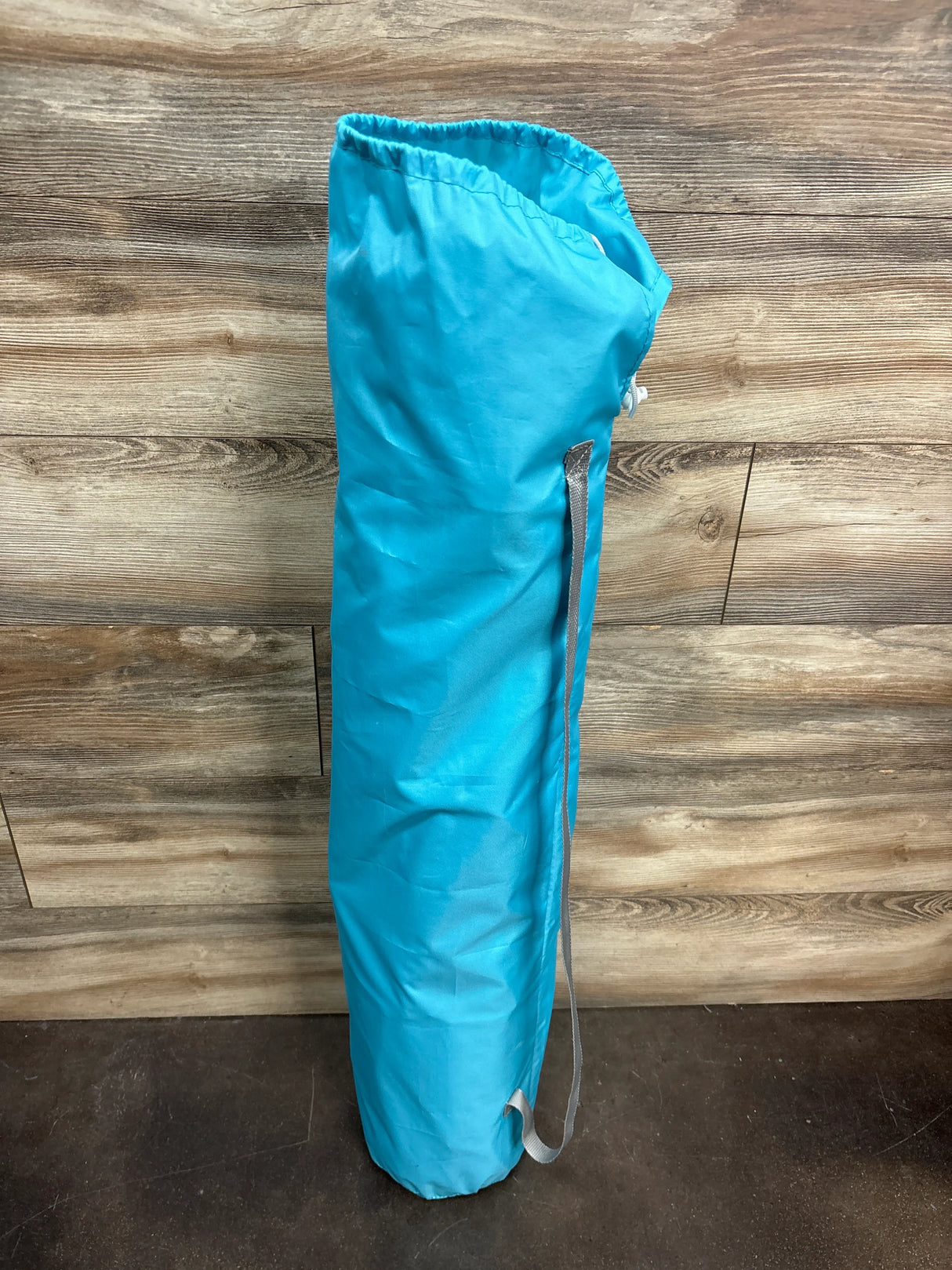 Blue camping gear bag with strap against wood panel wall and dark floor