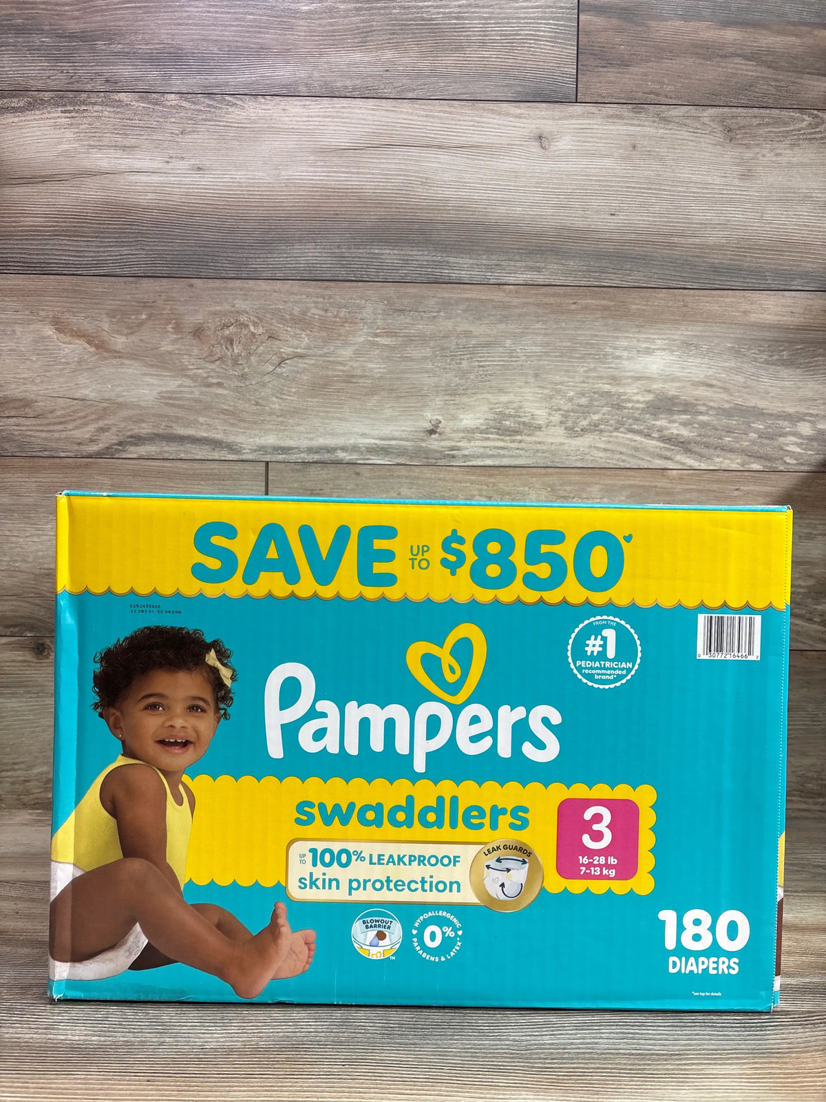 Front view of Pampers Swaddlers Size 3 diaper box showcasing 180 diapers and leakproof skin protection on a wood floor