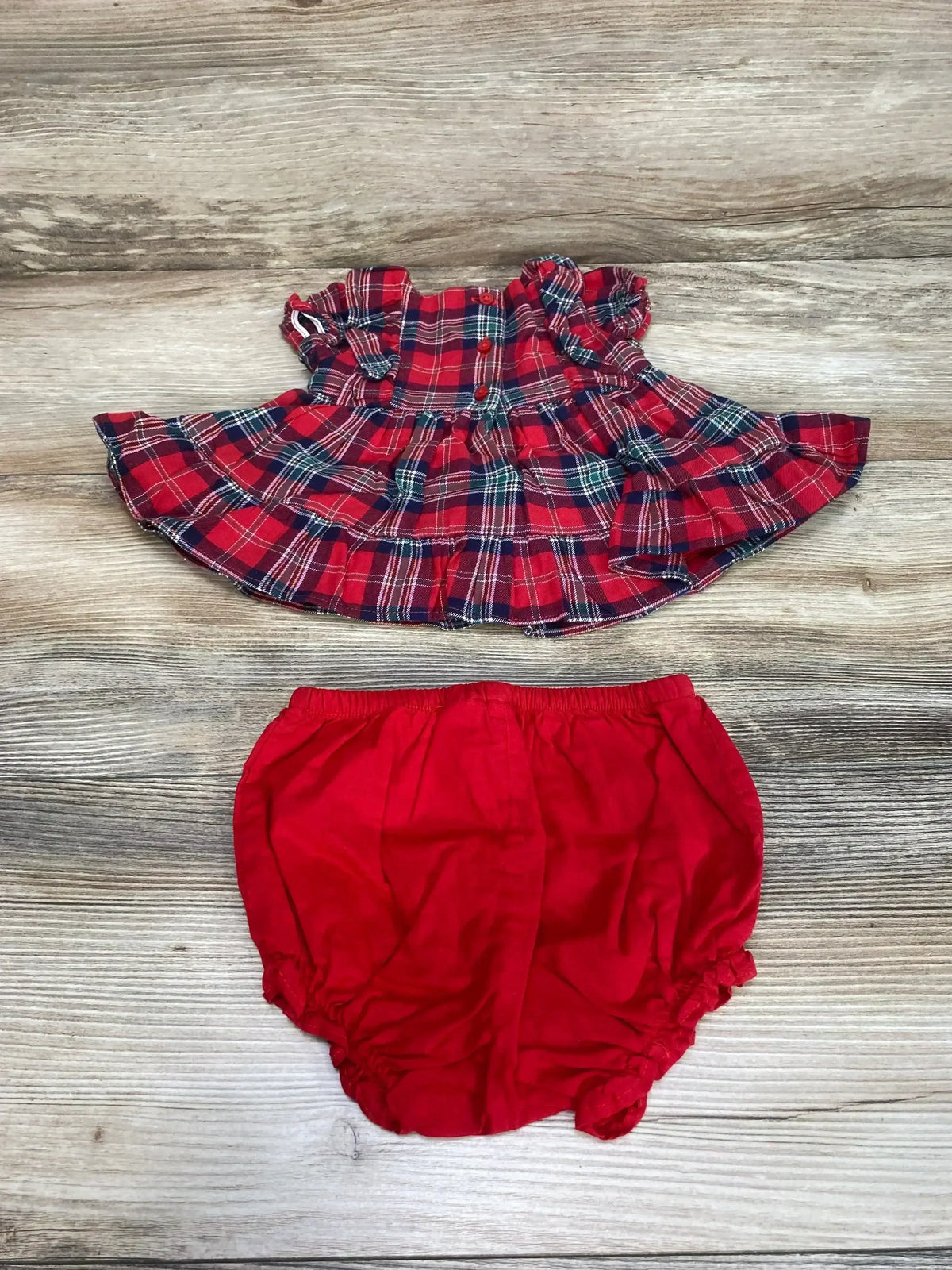 Flat lay of Janie & Jack 2-piece red plaid baby set showing ruffled short-sleeve plaid top and red elastic-waist bloomers on light wood background
