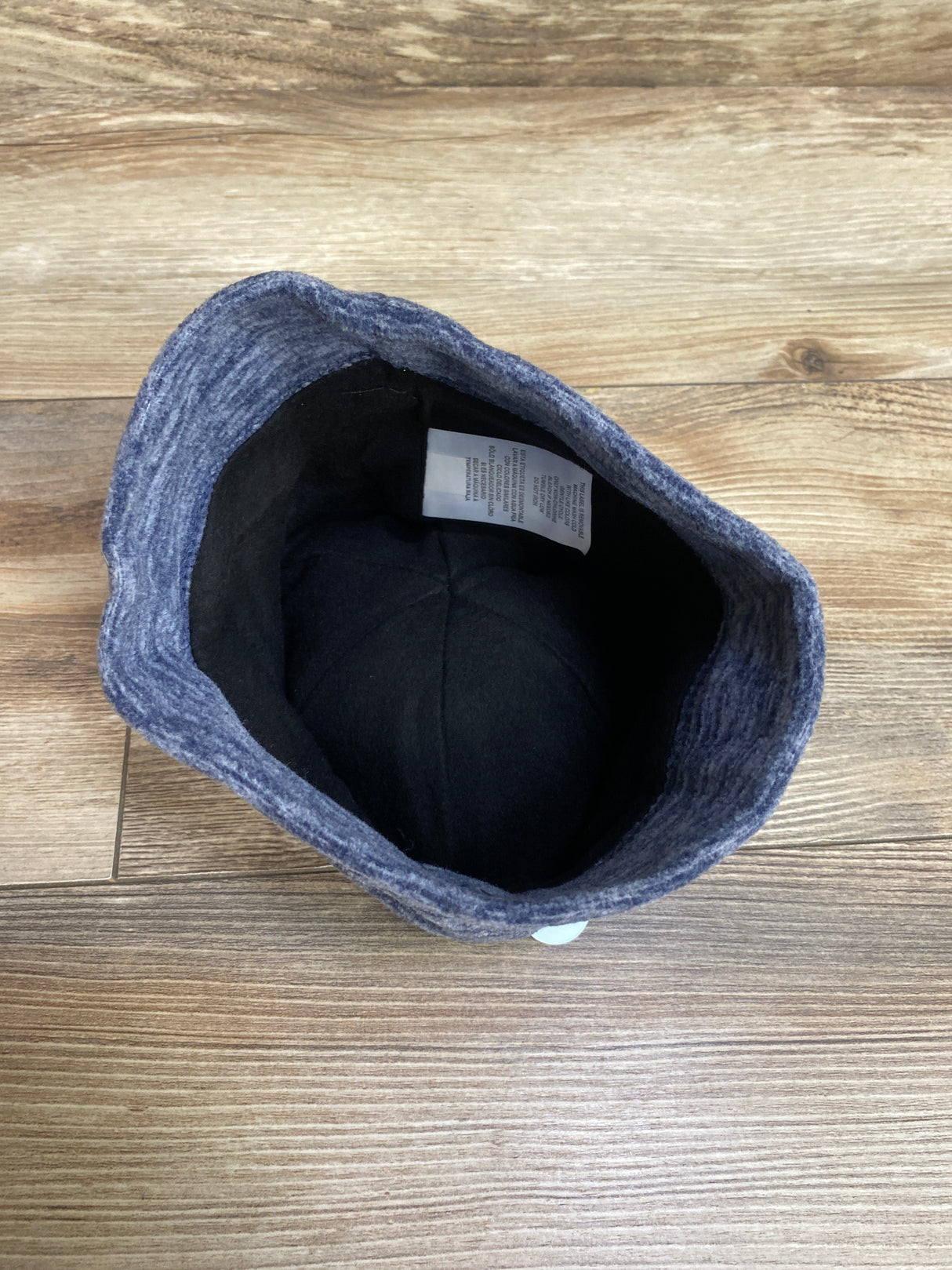Top view of a blue knitted hat with black interior lining placed on wooden floor