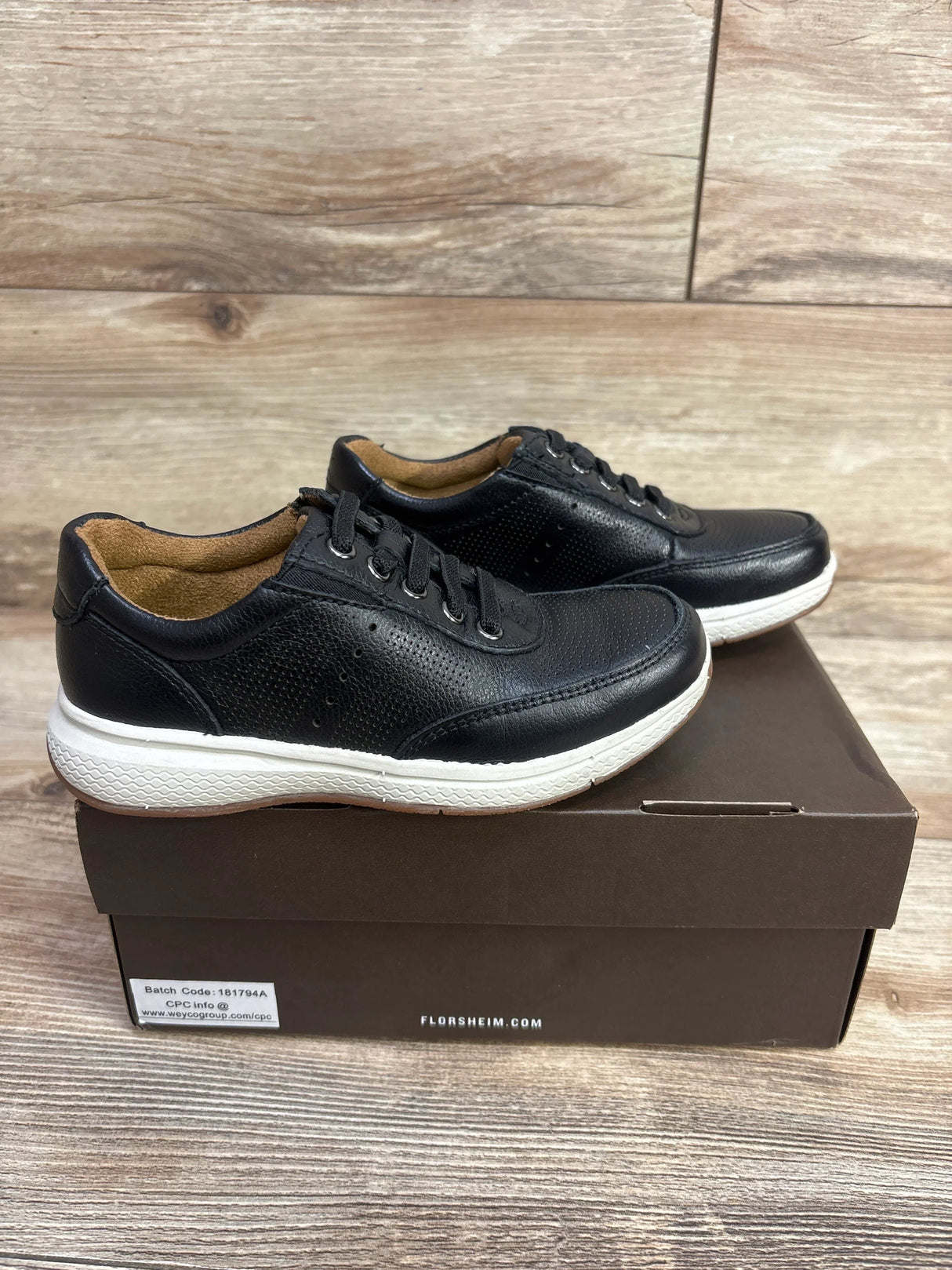 Black leather sneakers with white soles on a brown shoebox, wood background