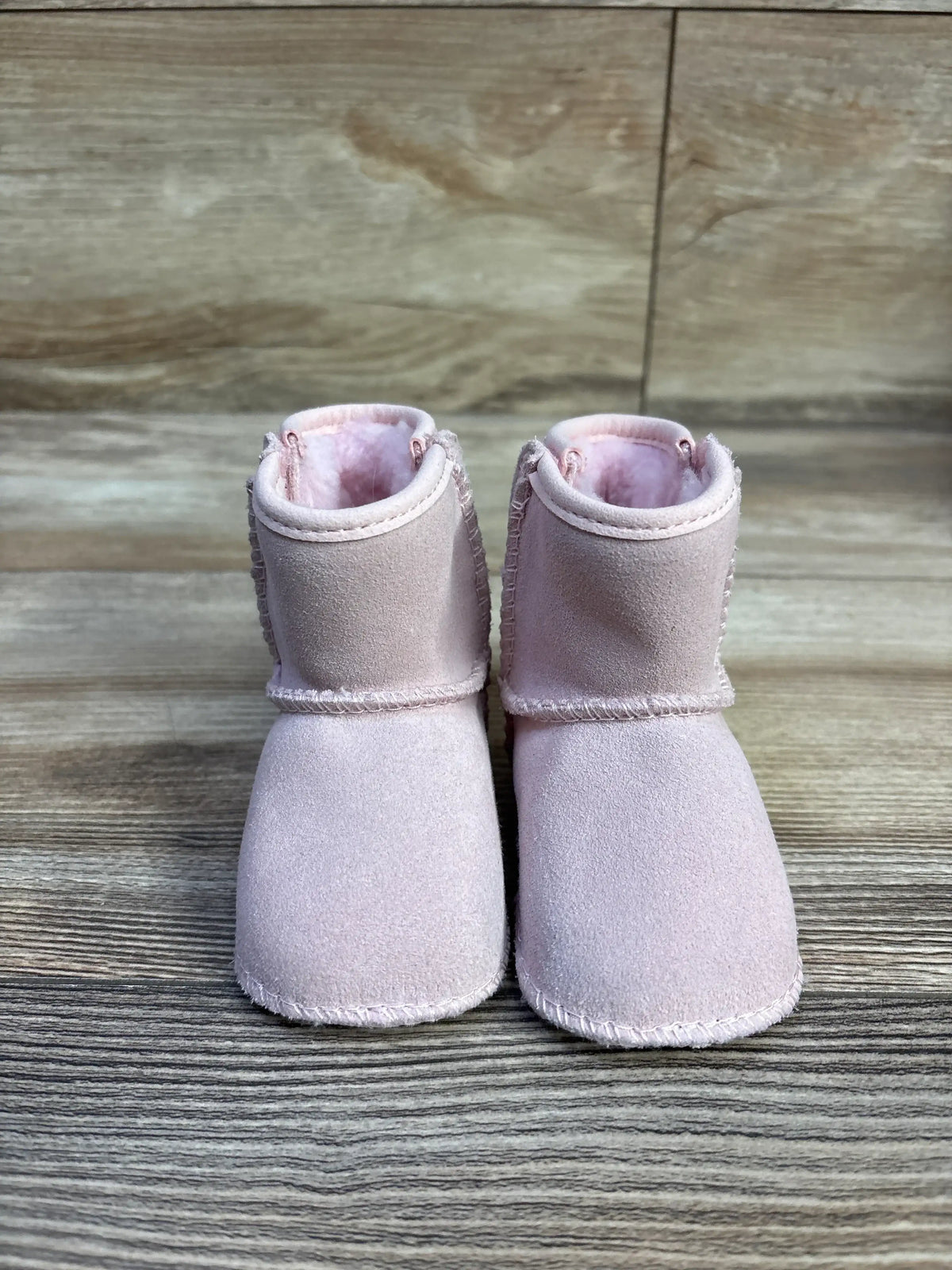 Front view of UGG Baby Classic Soft Sole baby boots in pink showing suede exterior and plush fleece lining on wood background