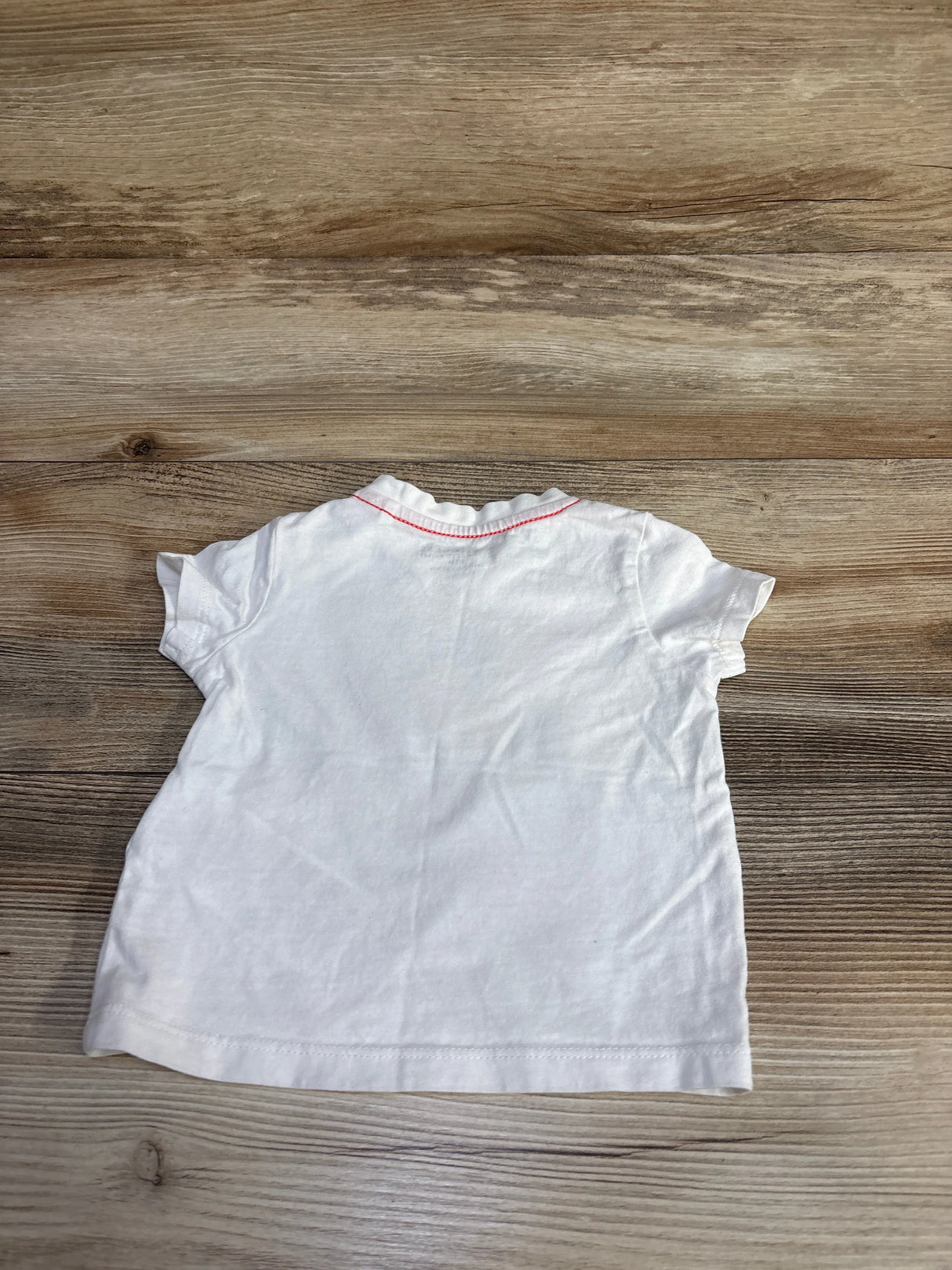 Back view of a white baby t-shirt with pink stitching on a wooden surface