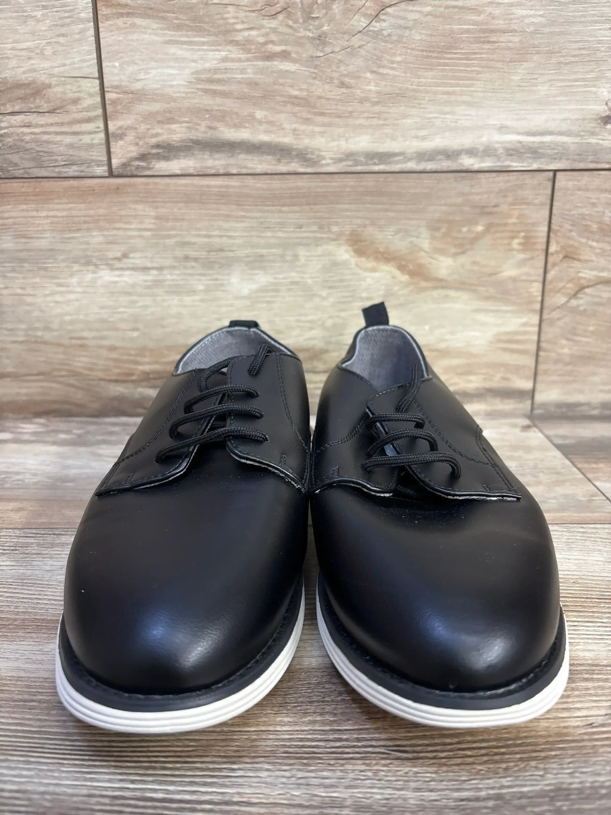 Front view of Cat & Jack Alfi dress shoes in black, size 6Y, showcasing lace closure and white soles on a wood-patterned surface