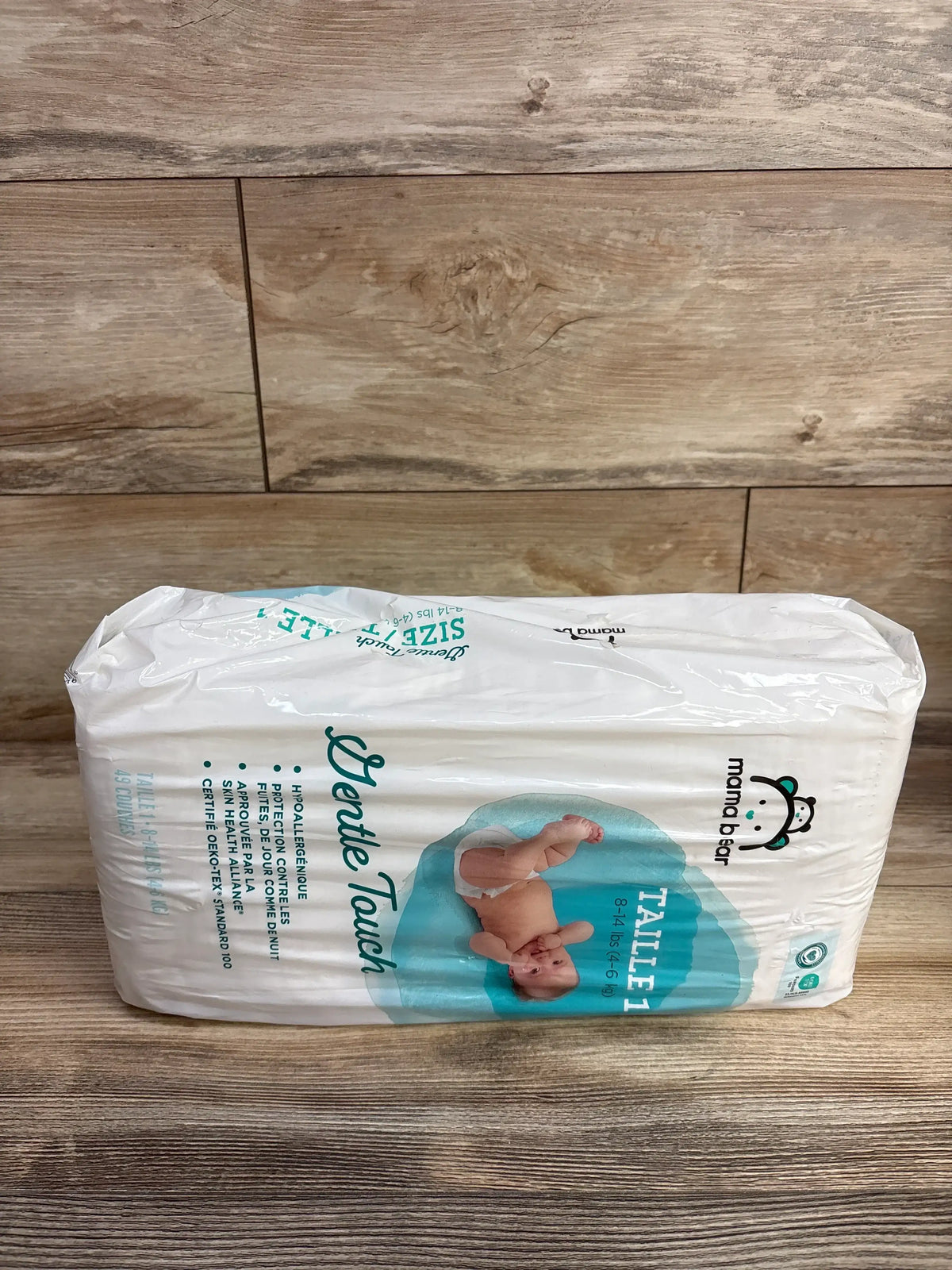 Side view of Mama Bear Gentle Touch Size 1 diaper pack showing baby photo and hypoallergenic claim on wooden tabletop