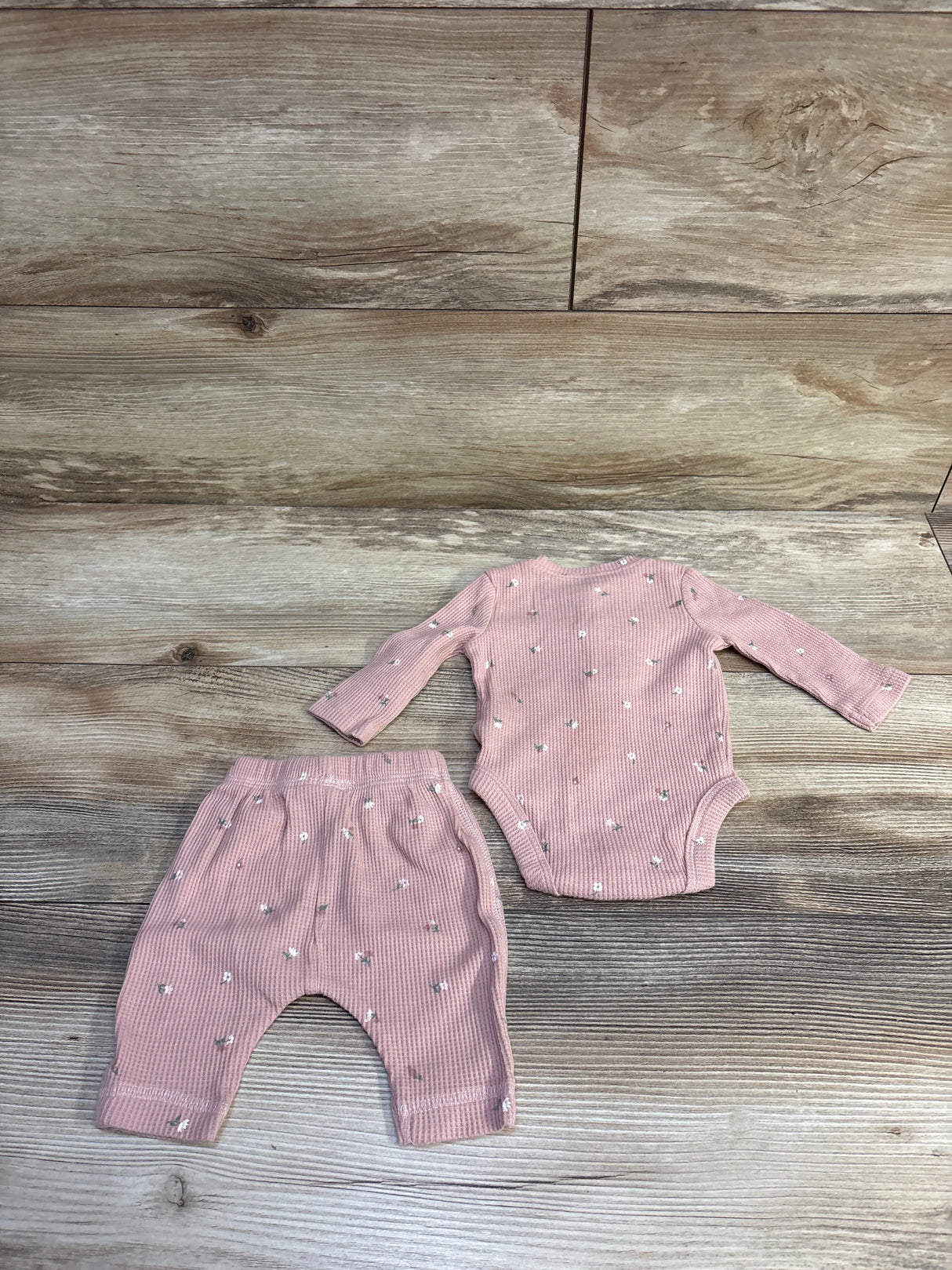 Flat lay of Carter’s newborn pink waffle-knit bodysuit and pants showing ribbed texture and small white flower print on wood