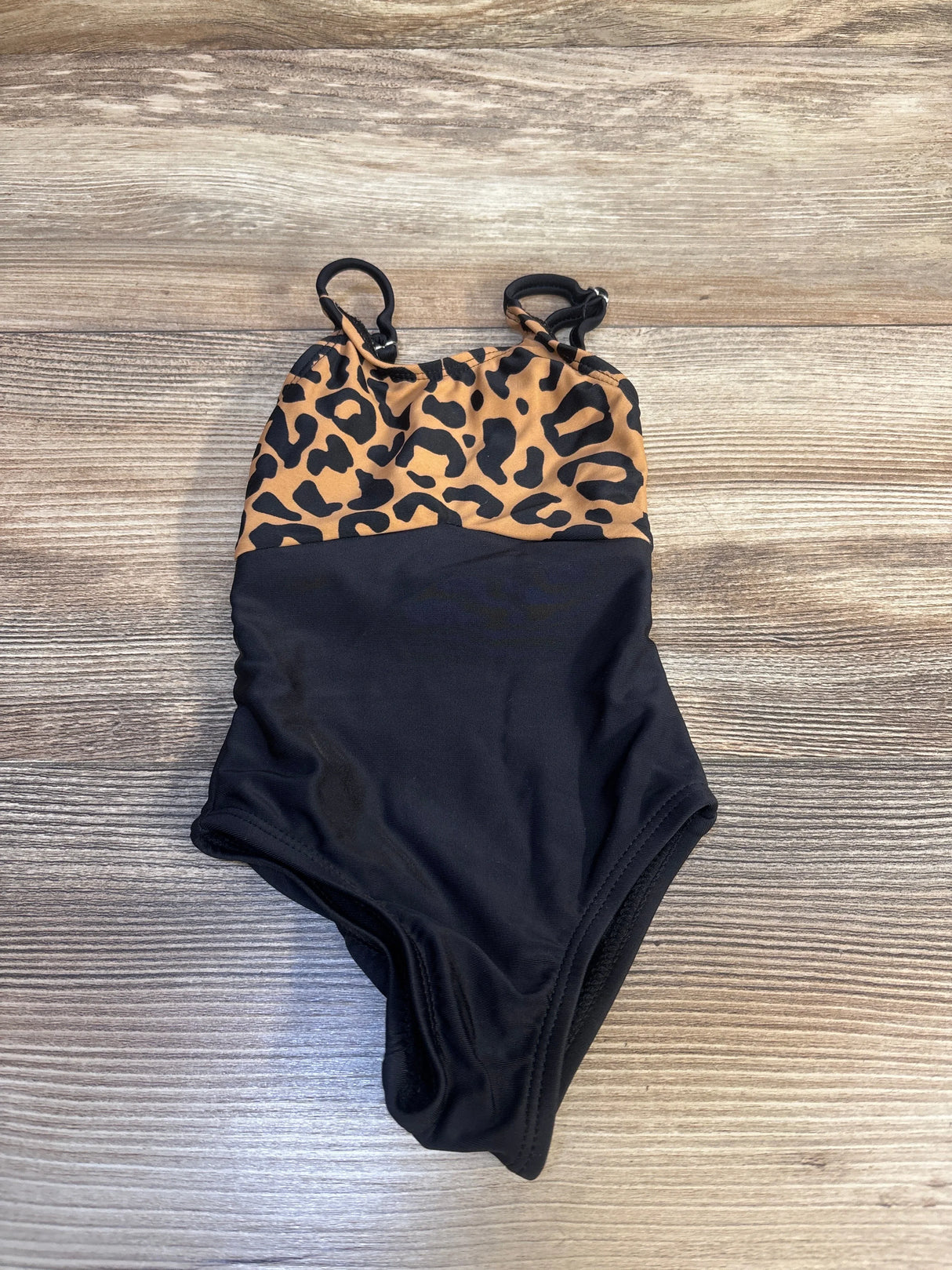 Kids one-piece swimsuit with leopard print top and solid black bottom on wood background