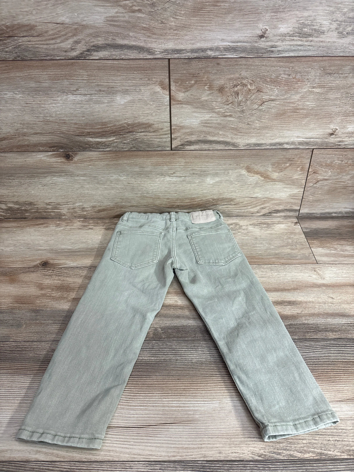 Back view of Zara The Regular toddler denim jeans in faded green showcasing back pockets and straight legs on wood background