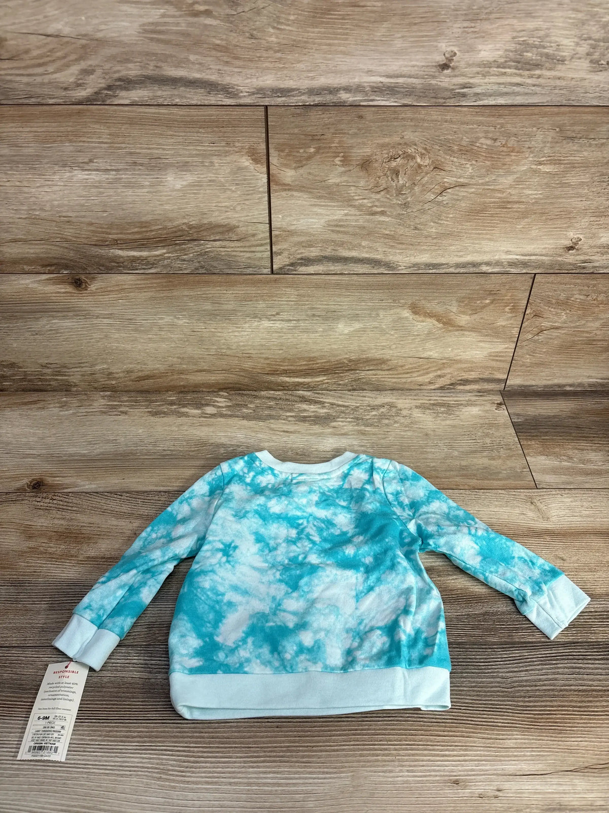 Baby long sleeve tie-dye blue and white shirt on wooden background with clothing tag attached