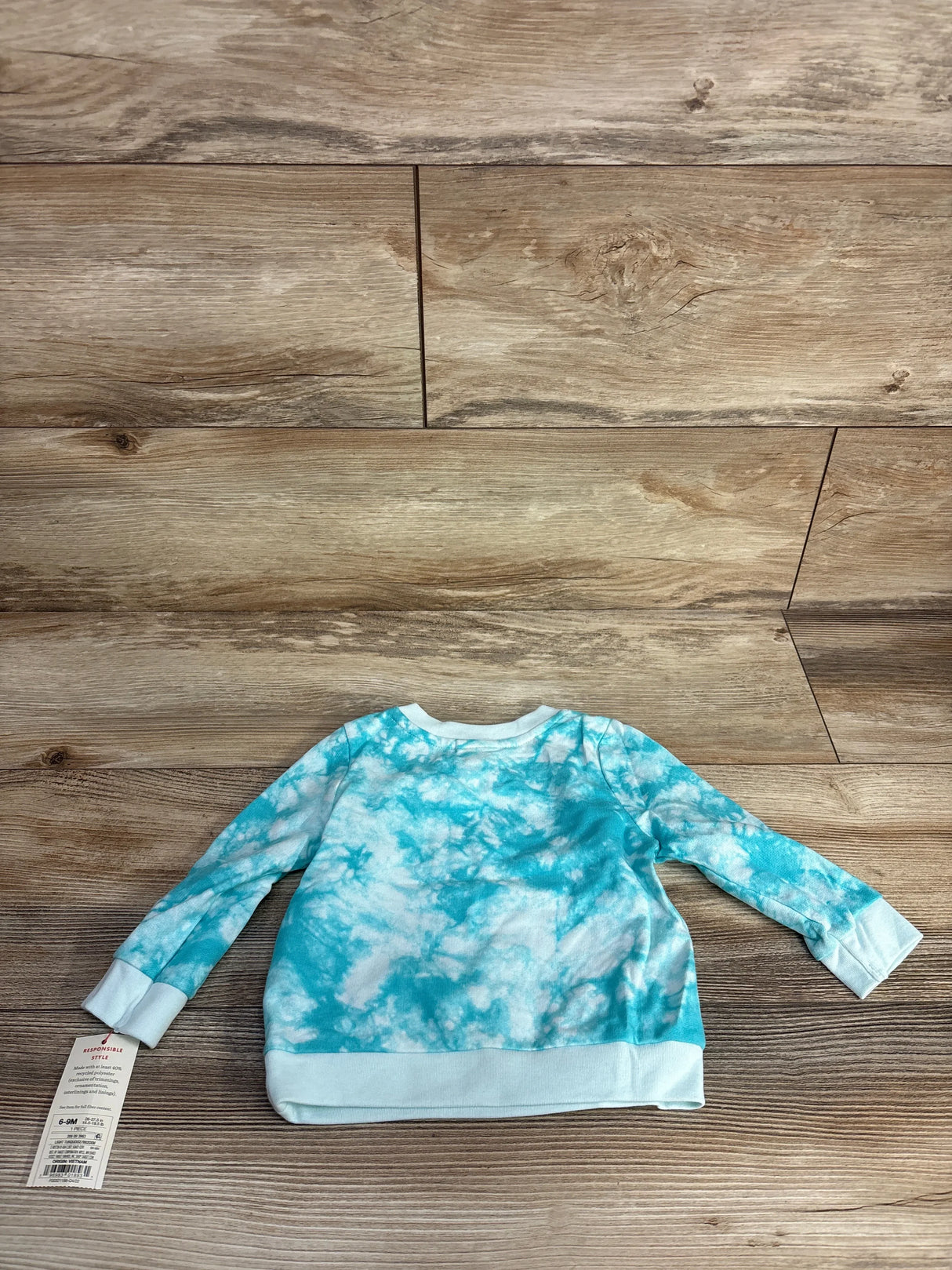 Baby long sleeve tie-dye blue and white shirt on wooden background with clothing tag attached