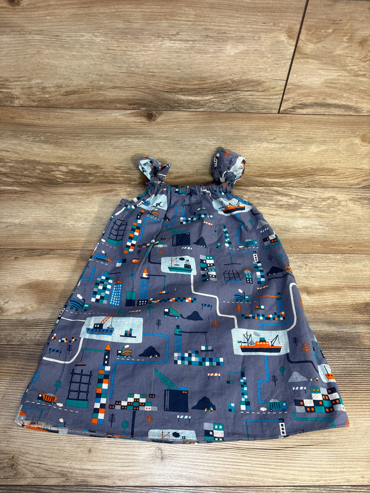 Gray baby dress with city map print, construction trucks, boats, and buildings on wood floor